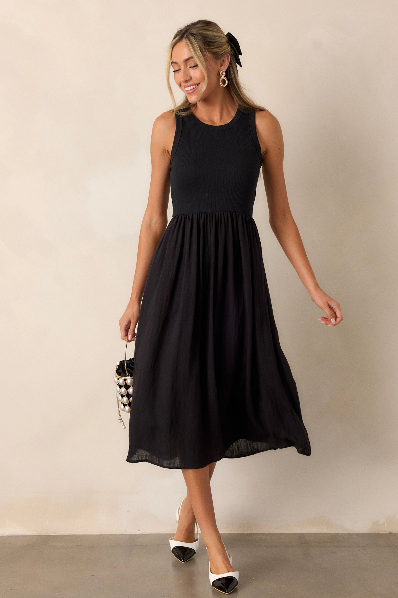 Movement view of this sleeveless black dress that features a crew neckline, a stretchy ribbed bust, a cinched waist, and flowing mid-length skirt.