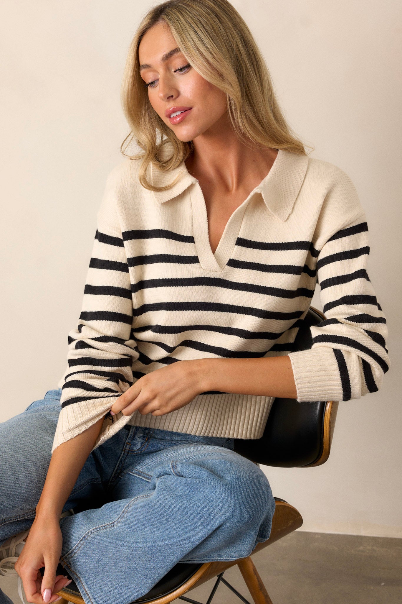 This beige sweater features a v-neckline with a collar, classic black horizontal stripes, long sleeves, and a ribbed hem and cuffs.