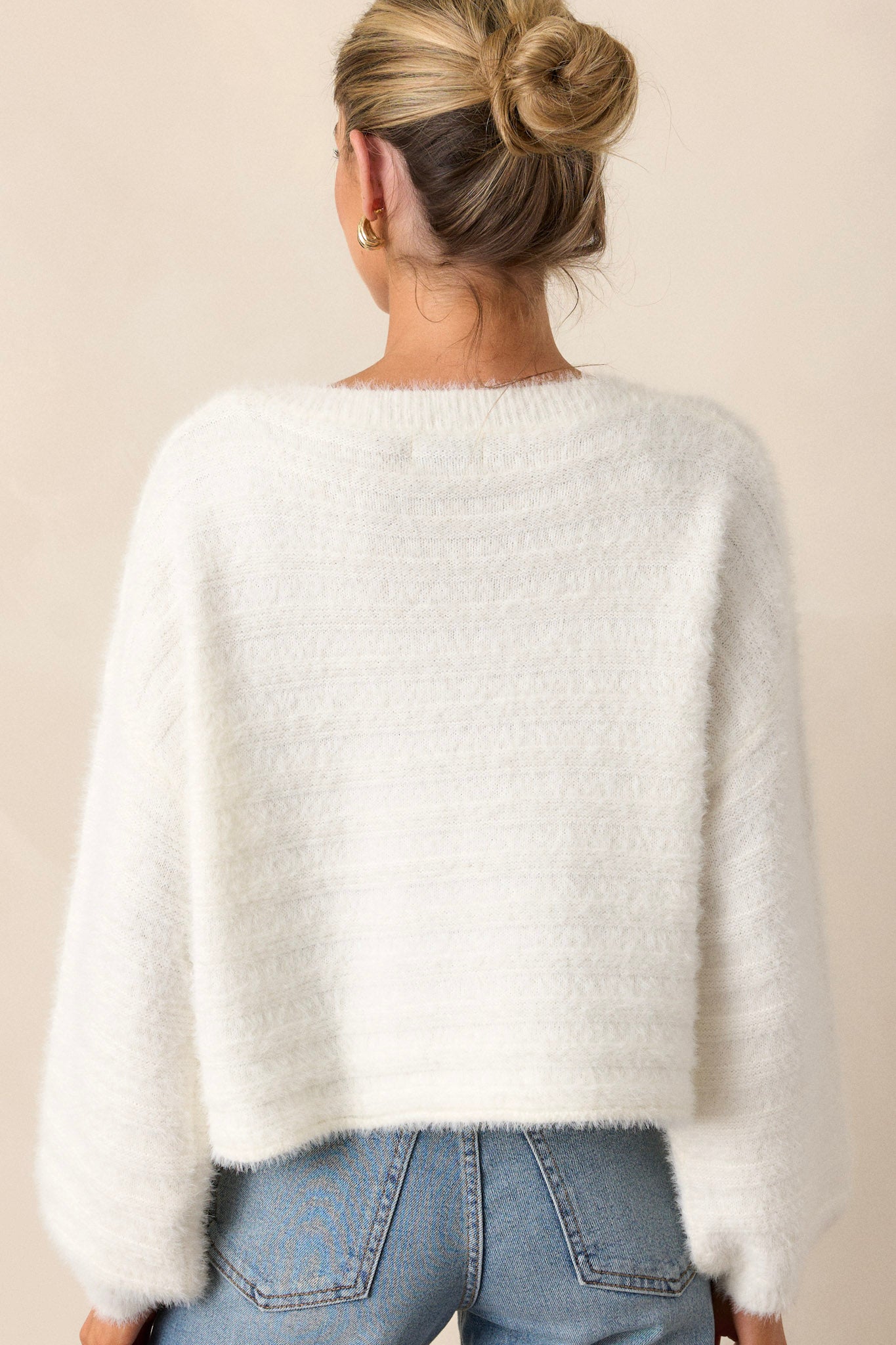 A back view of the sweater, showcasing the smooth lines and ribbed texture extending along the back, highlighting the slightly cropped length.