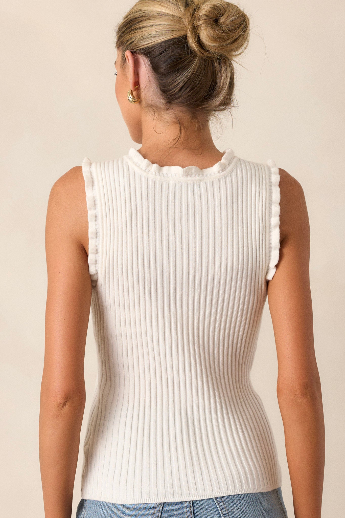 Back view of an ivory ruffle knit tank top highlighting the overall fit, sleeveless design, and ruffle trim.