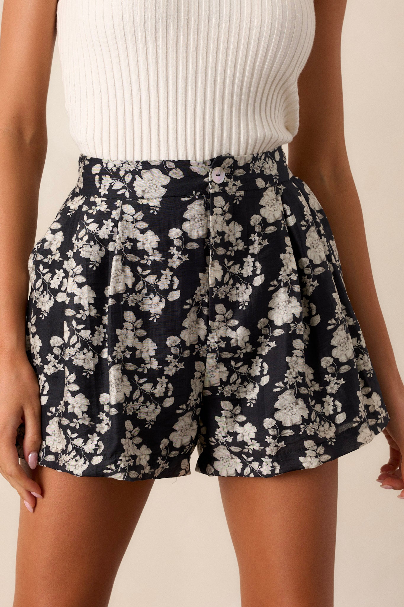 Close-up view of these black shorts that feature a fun ivory floral print, with a front button closure, and two functional pockets.