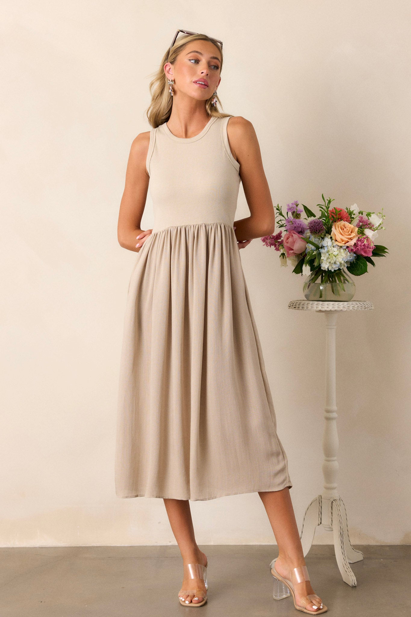 Full body of this sleeveless tan dress that features a crew neckline, a stretchy ribbed bust, a cinched waist, and flowing mid-length skirt.