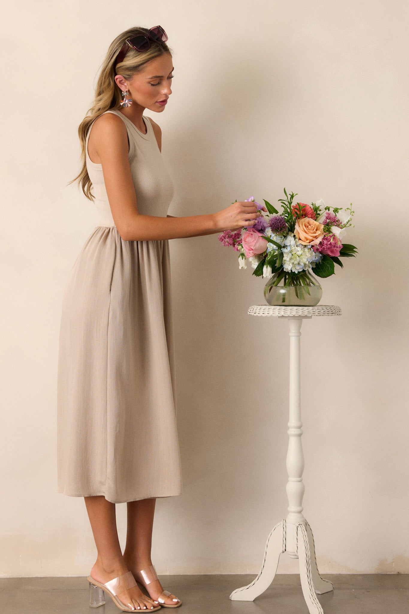 This sleeveless tan dress features a crew neckline, a stretchy ribbed bust, a cinched waist, and flowing mid-length skirt.