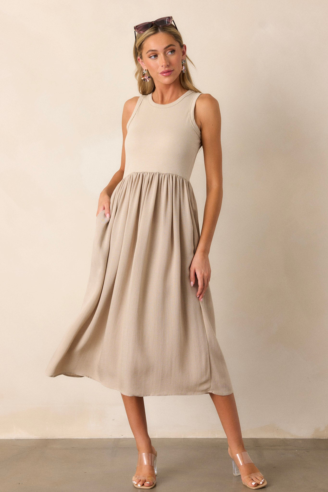 Angled view of this sleeveless tan dress that features a crew neckline, a stretchy ribbed bust, a cinched waist, and flowing mid-length skirt.