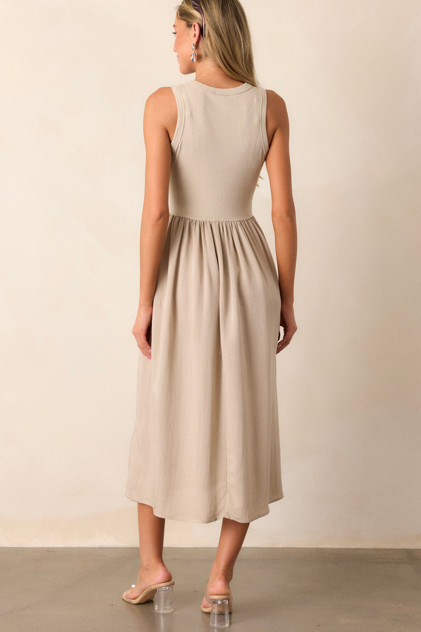 Back view of this sleeveless tan dress that features a crew neckline, a stretchy ribbed bust, a cinched waist, and flowing mid-length skirt.