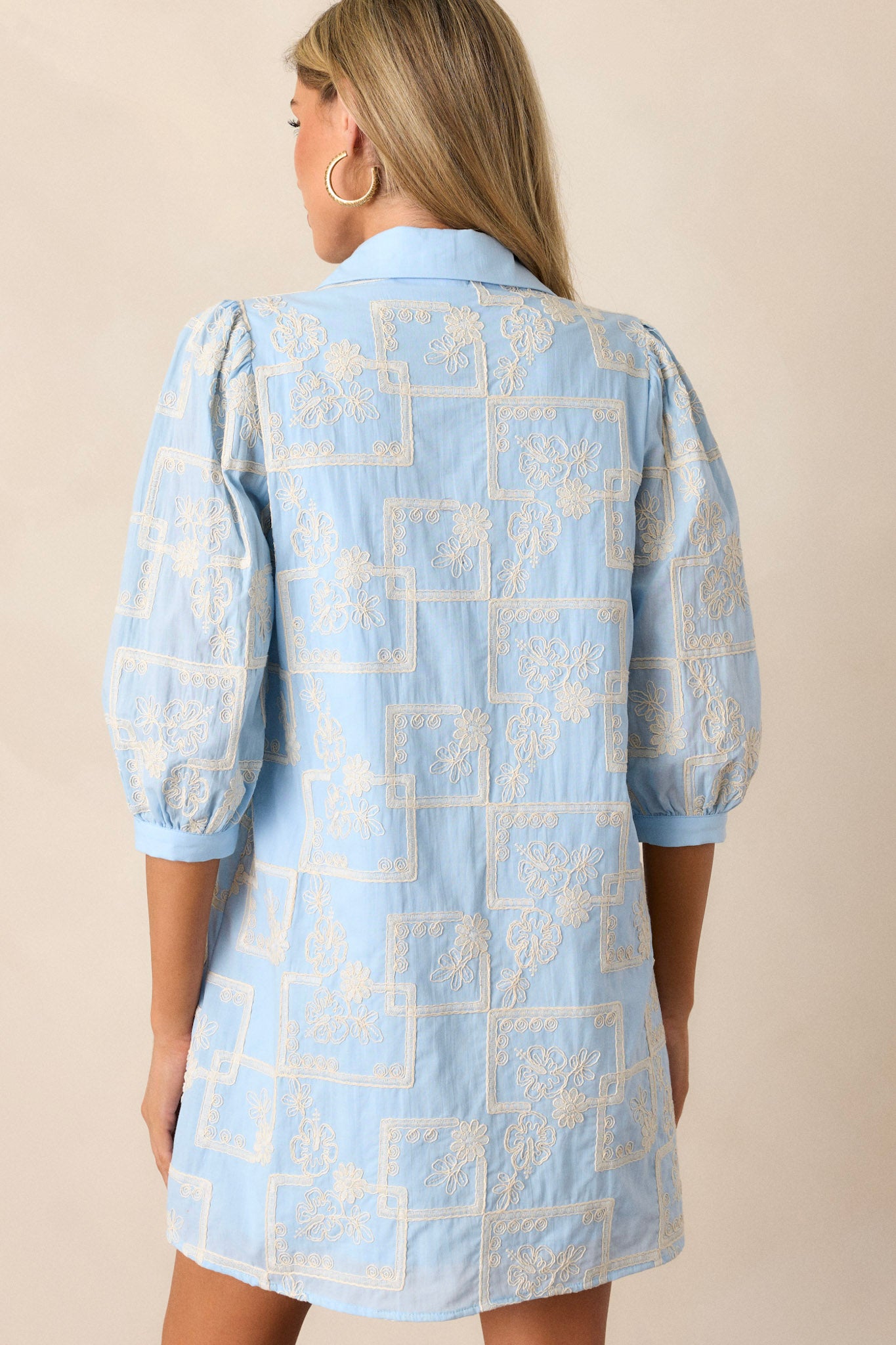 Back view of this dress that features a collared neckline, a functional button up bust, a white embroidered floral and square pattern, a relaxed fit and puffed half sleeves.