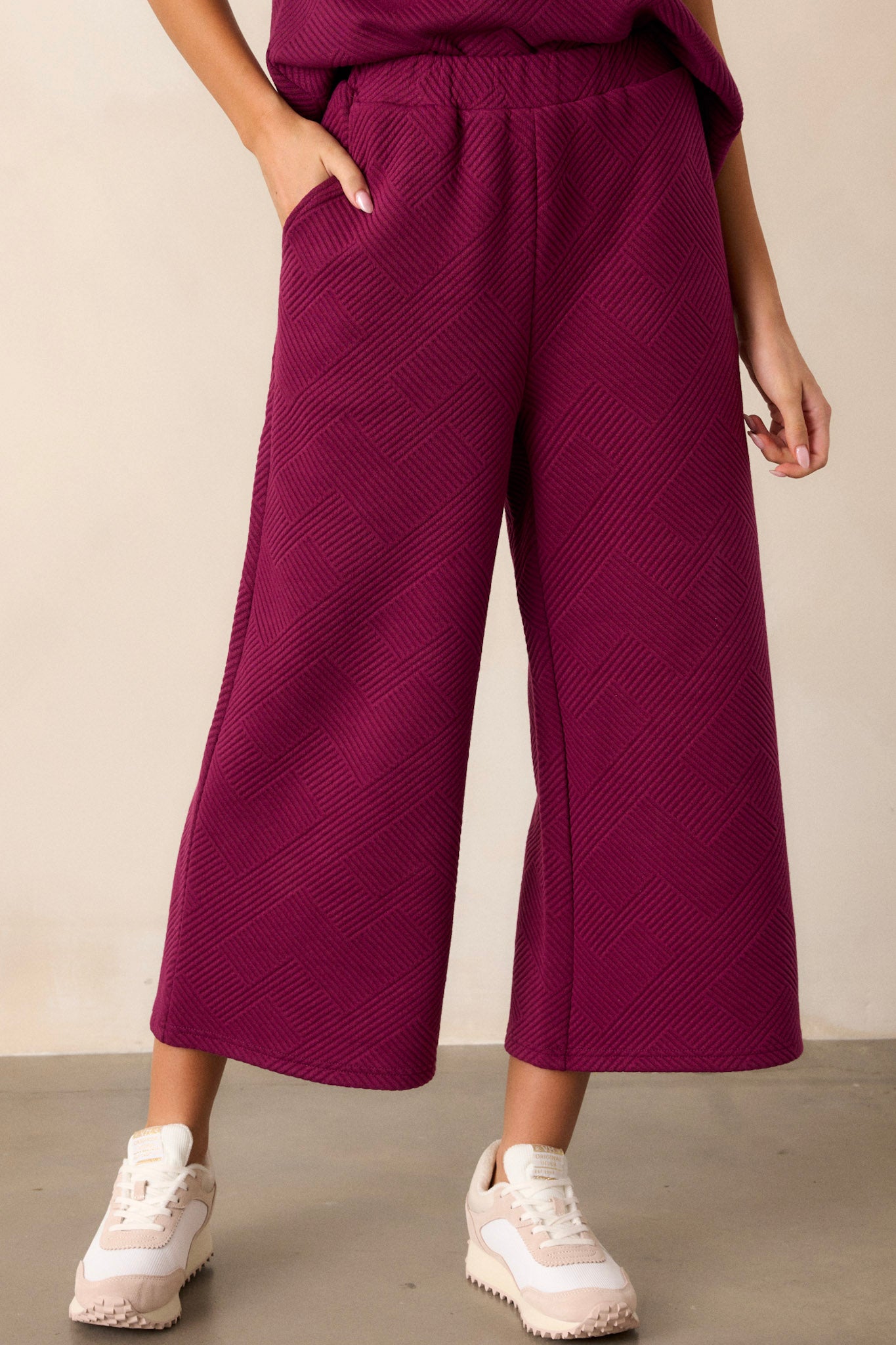 Front view of sangria purple pants featuring a high waisted design, an elastic waistband, functional hip pockets, a textured crisscross design, and a wide leg.