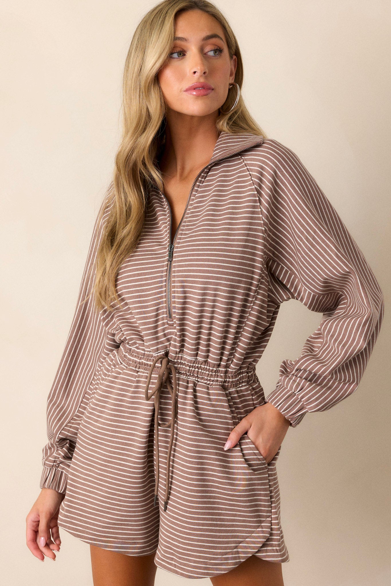 Front angled view of this mocha stripe romper that features a collared neckline, a functional front zipper, a brown & ivory striped design, an elastic waistband, functional hip pockets, a waist drawstring and long sleeves.