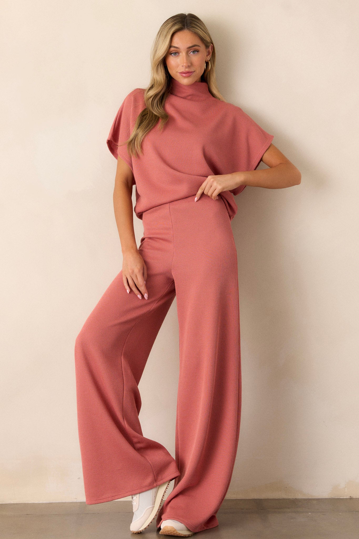 Full body view of this coral top that features a turtleneck, a knit towel like texture on the outside, a soft smooth inside, cinching in the hips and short flowy sleeves.