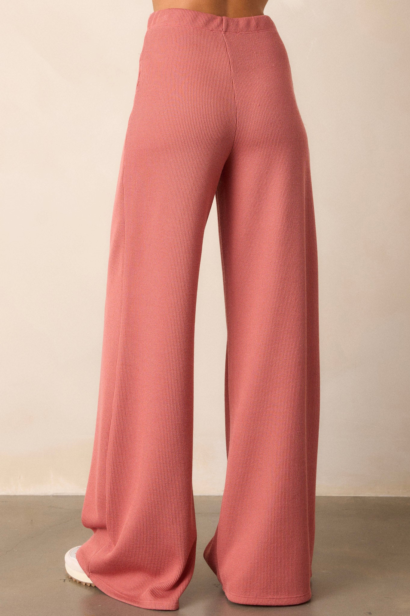 back view of these coral knitted pants that feature an elastic waist band, a high waisted design, a knit towel like texture on the outside, a soft inside and a wide leg.