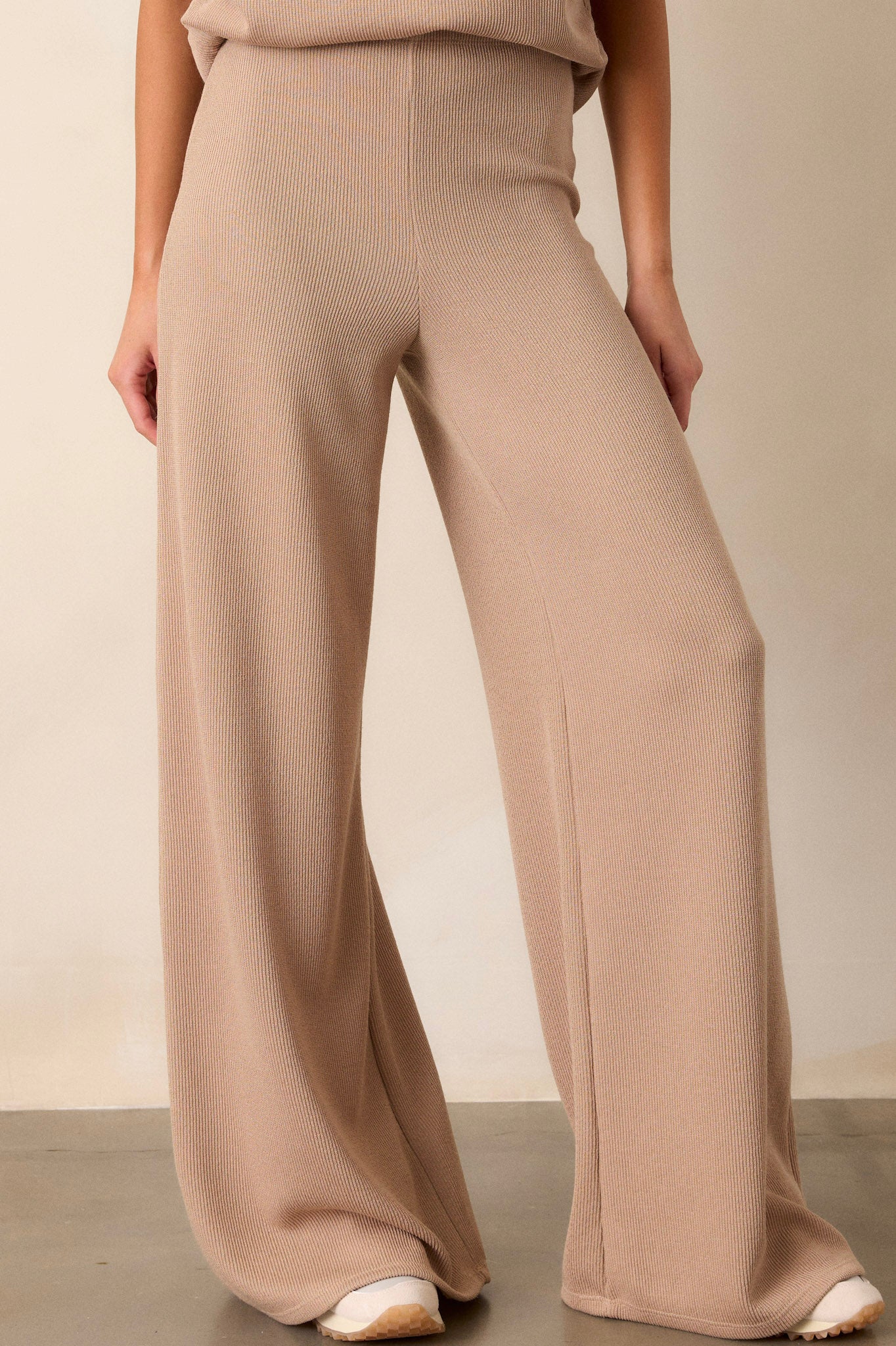 Front angled view of the beige knitted pants featuring an elastic waistband, a high-waisted design, a knit towel-like texture on the outside, a soft inside, and a wide leg