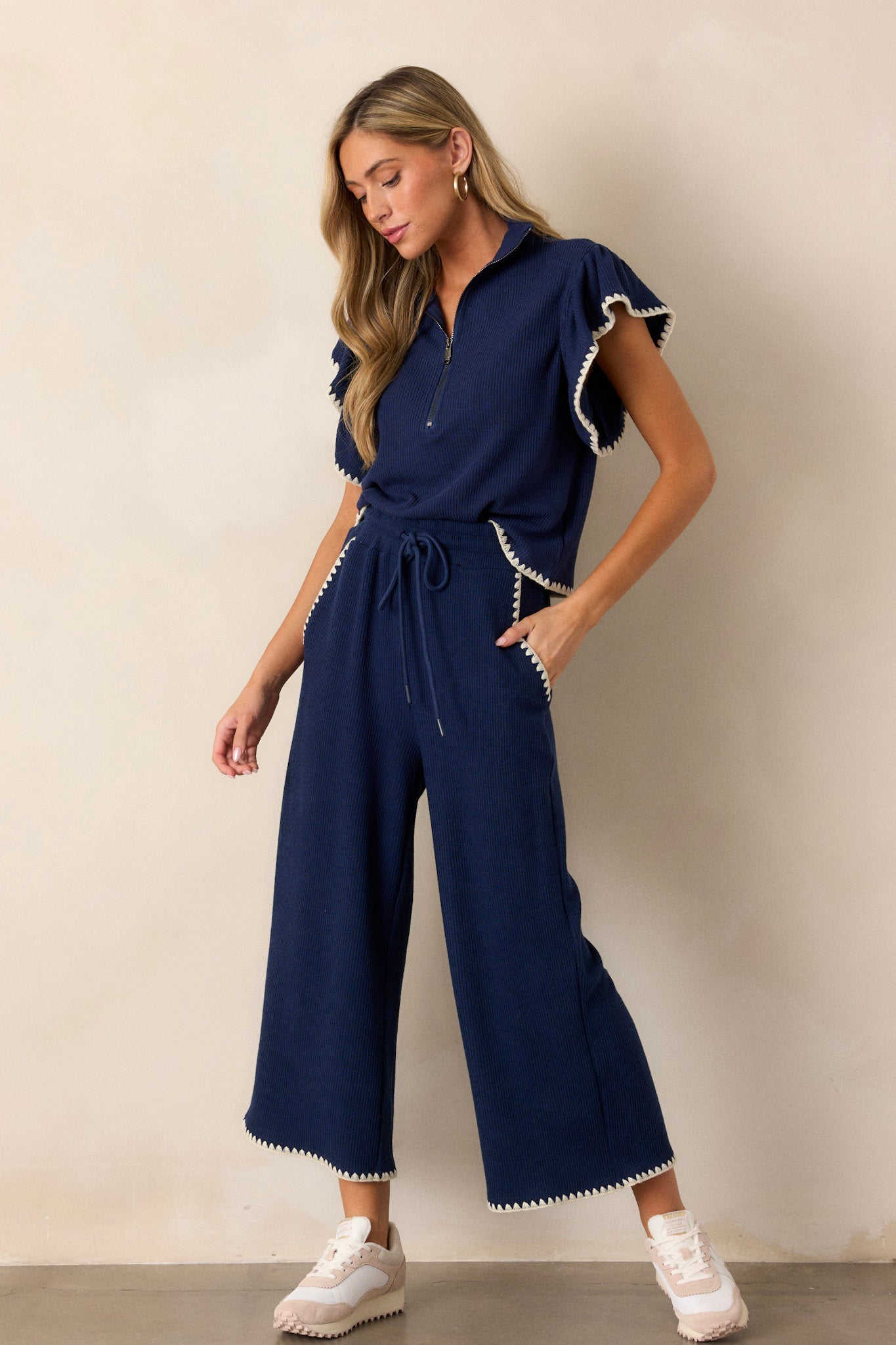 These navy pants feature an elastic waistband, an adjustable drawstring, ivory blanket stitch detailing, functional hip pockets, a soft knit material, and a wide leg.