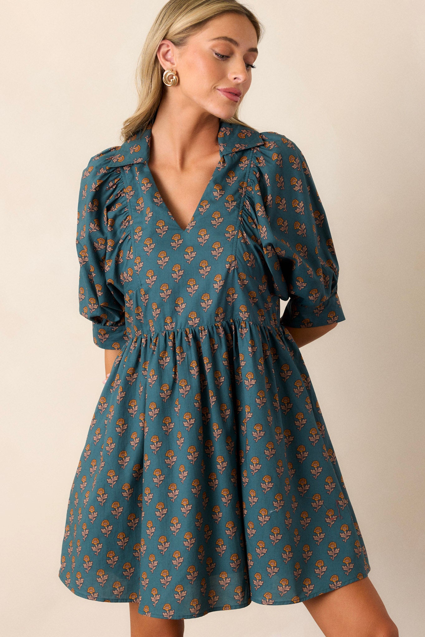 Front view of a teal dress featuring a small v-neckline, puff sleeves, and side pockets