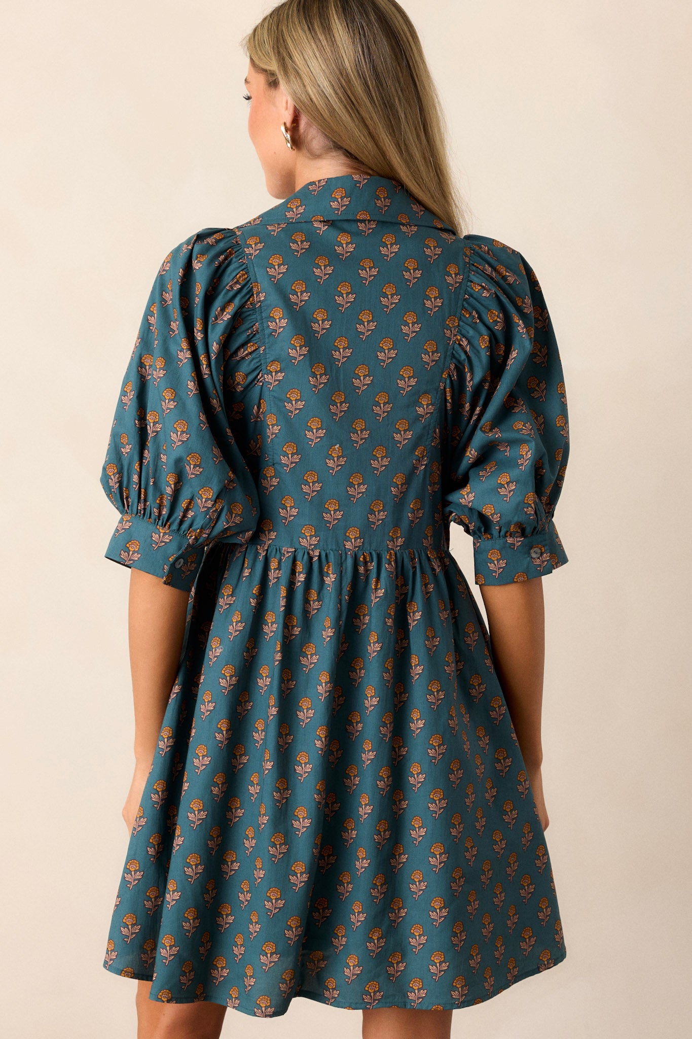 Back view of the teal dress highlighting the puff sleeves and the flow of the fabric down to the hemline.