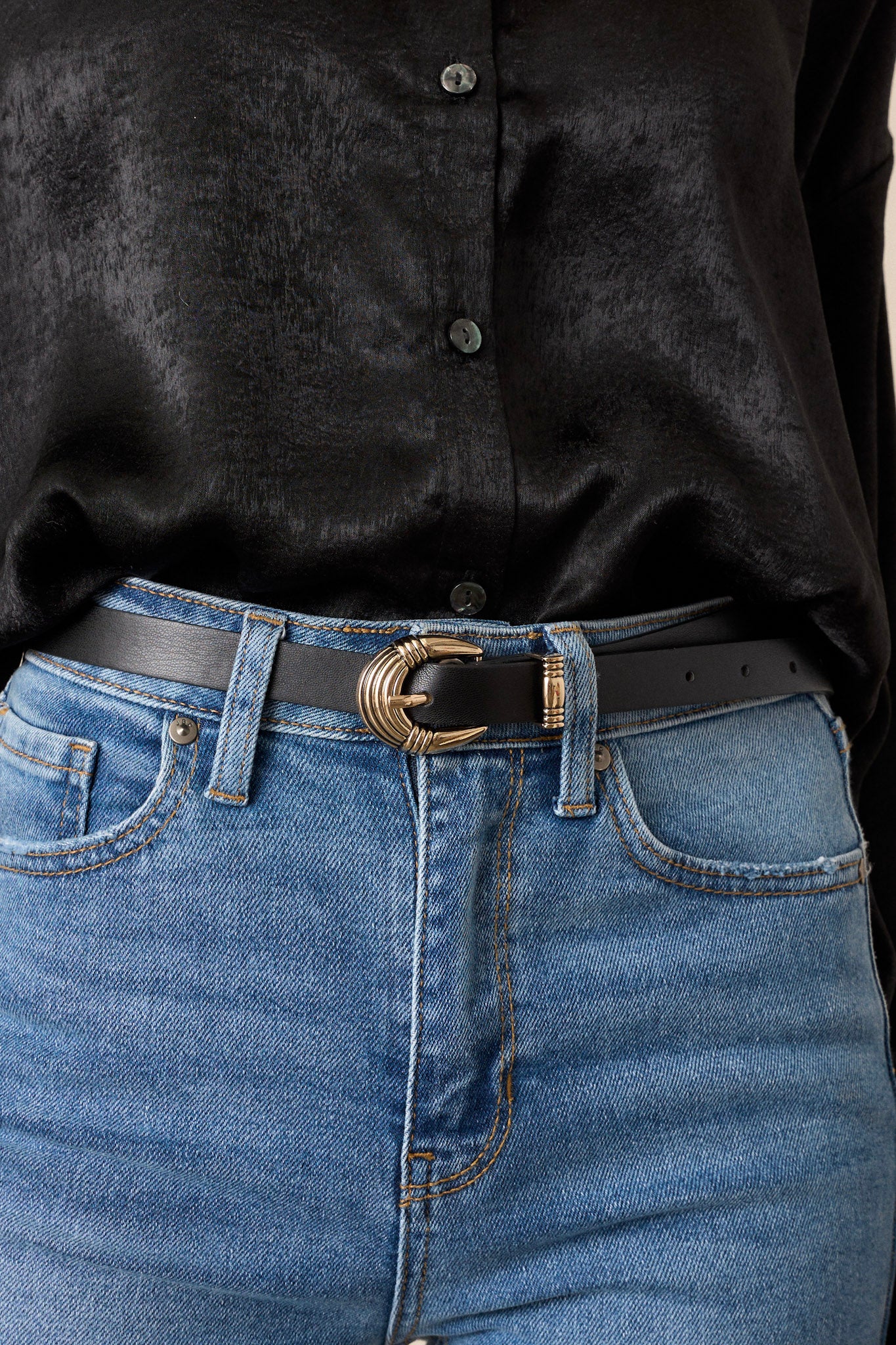 Close up of a black belt that features gold hardware, a pin buckle, and a faux leather material.