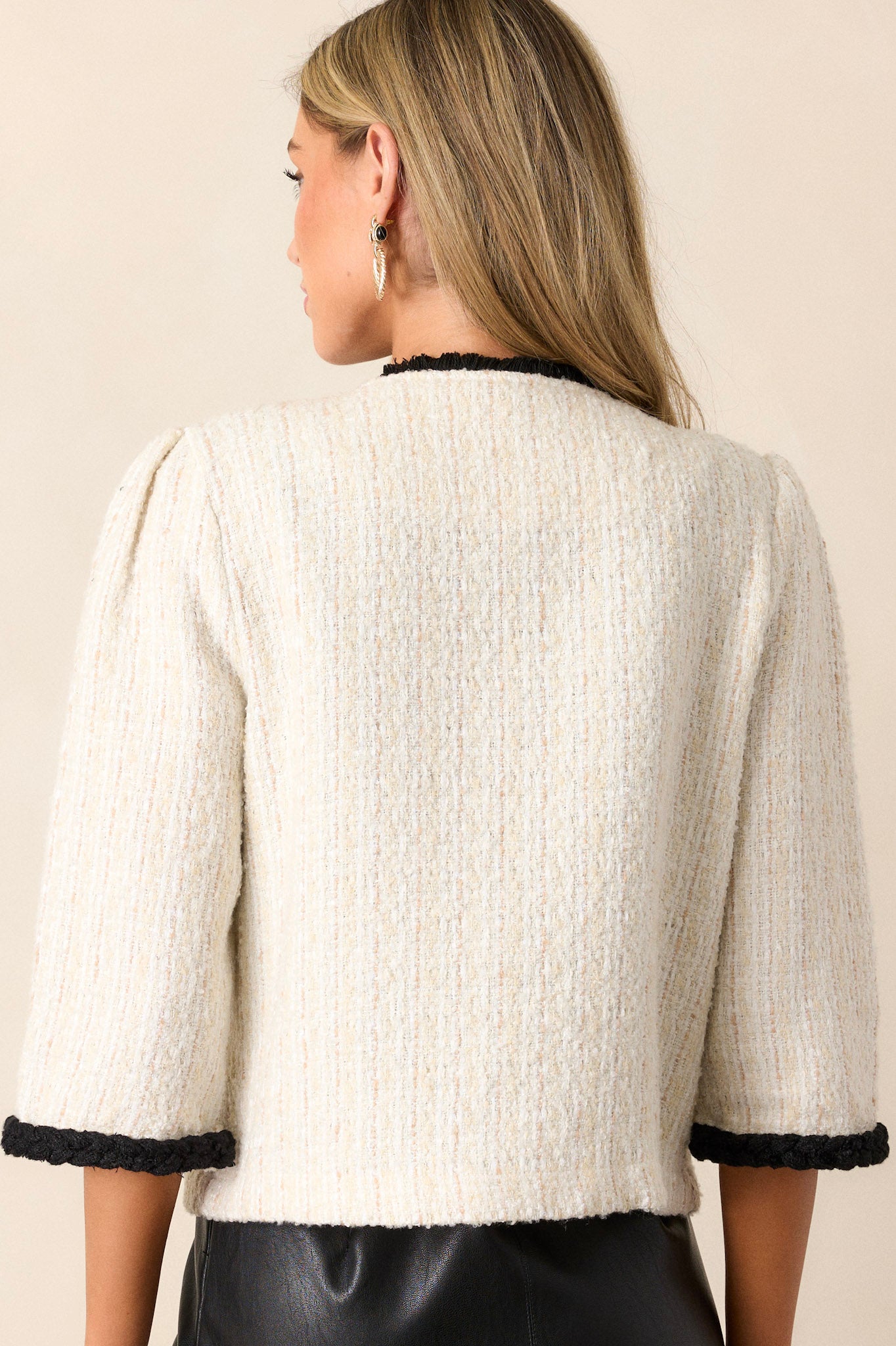 Back view of this ivory tweed jacket featuring a v-neckline, a functional button front, decal chest pockets, functional hip pockets, gold accent buttons and black trim.