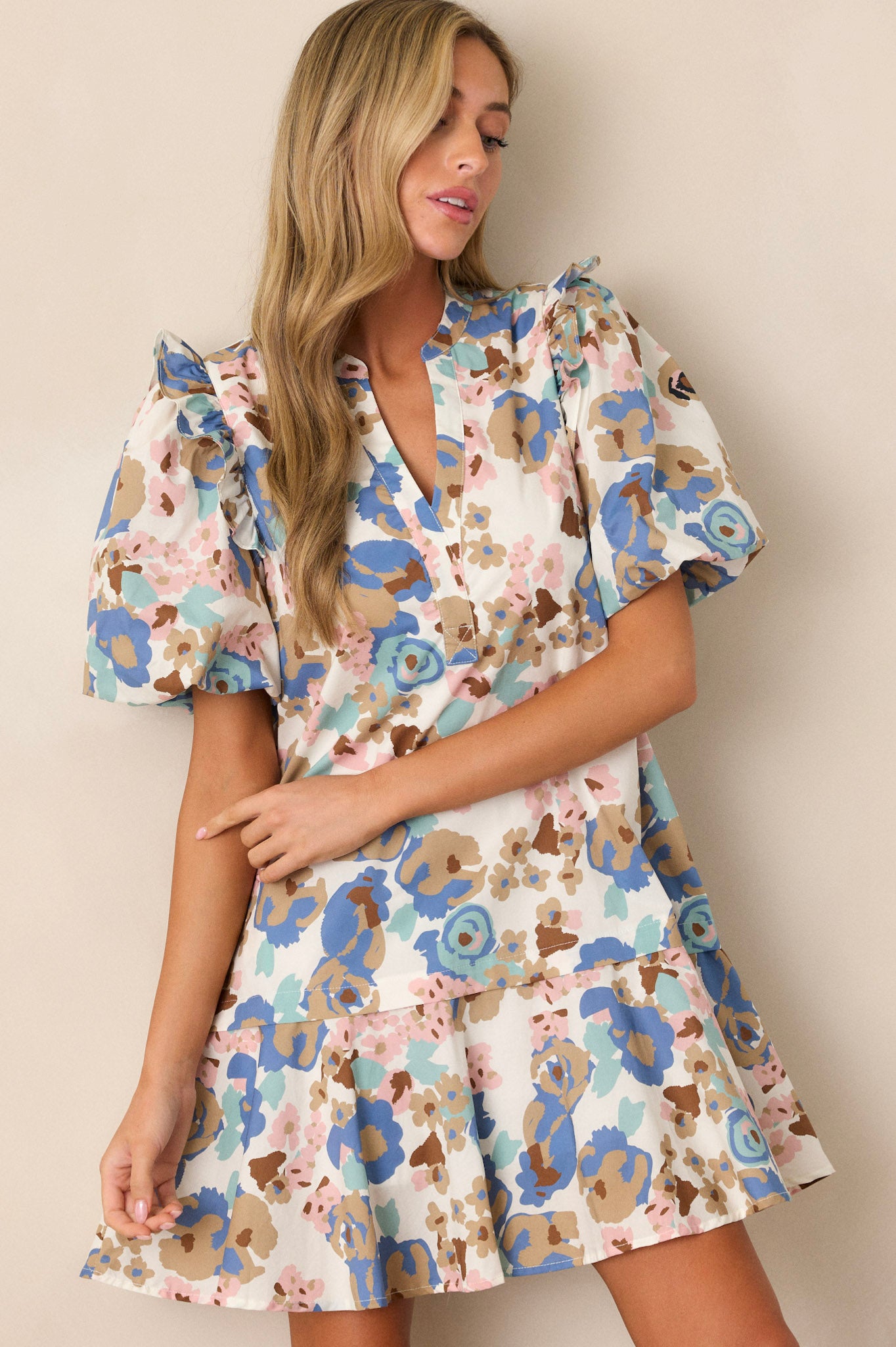 Front angled view of this ivory floral dress that features a slight v-neckline, a relaxed fit, a multi color floral pattern, functional hip pockets, a tiered design, a ruffled thick hemline and short elastic cuffed puff sleeves.