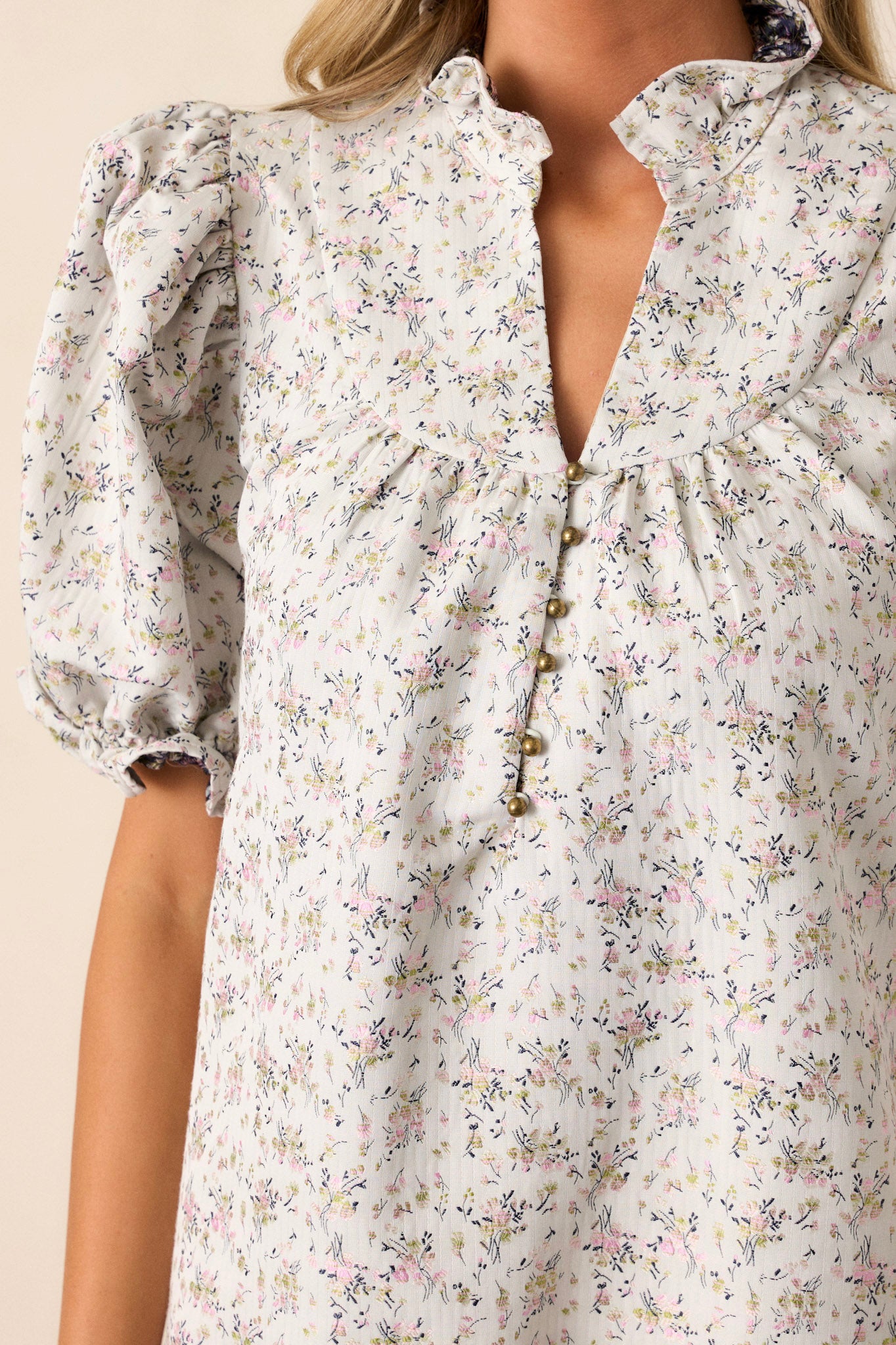 Front view of this almond floral dress that features a ruffle collared neckline, a split neckline with a functional button up bust, a soft quilt texture, a small floral pattern, a tiered design, a ruffled trim and short elastic cuffed puff sleeves.