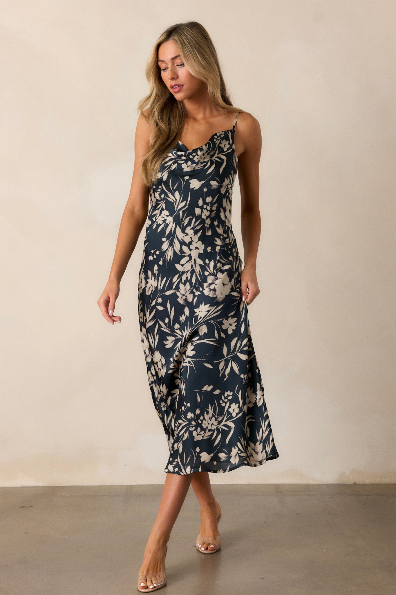 Full-length view of a dark teal dress featuring a cowl neckline, adjustable spaghetti straps, an ivory floral print, and a graceful midi length