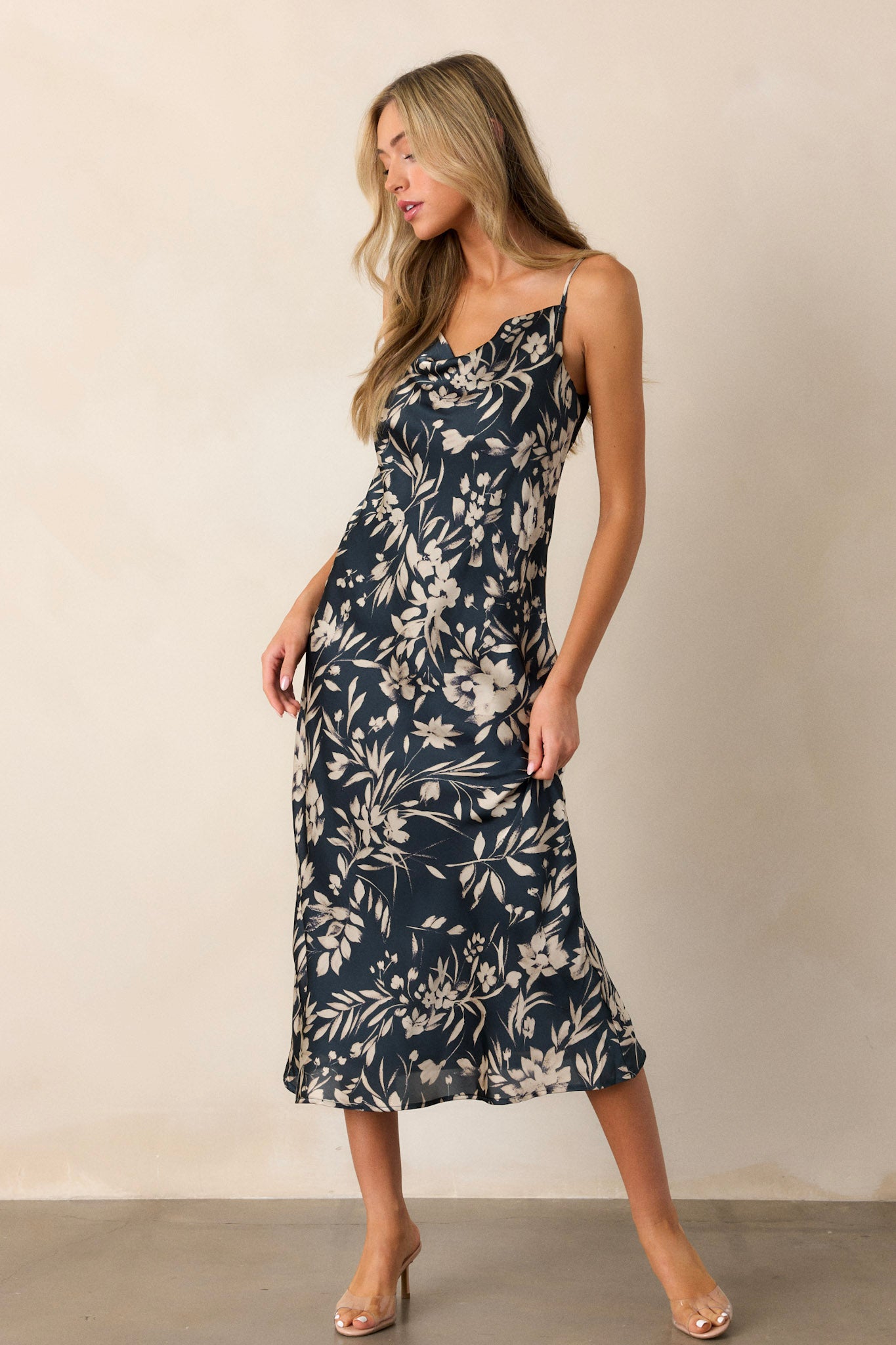 Angled view of the dark teal dress emphasizing the flow of the fabric, the elegant cowl neckline, and the ivory floral print scattered across the midi-length skirt