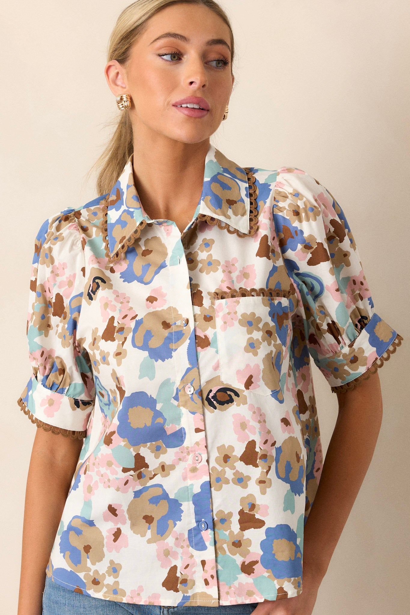 Front view of this ivory floral top that features a collar with brown detailing, puff sleeves, a front functional pocket and a functional button-front.