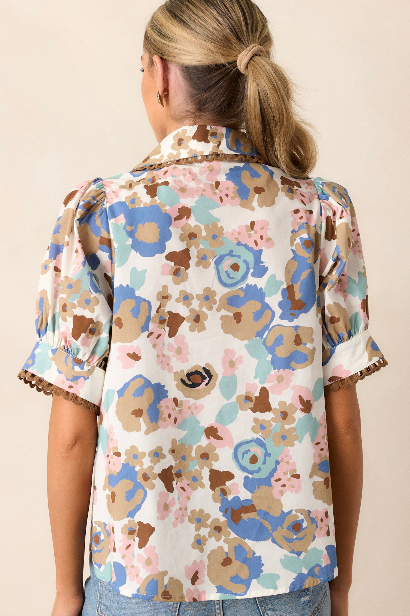 Back view of this ivory floral top that features a collar with brown detailing, puff sleeves, a front functional pocket and a functional button-front.