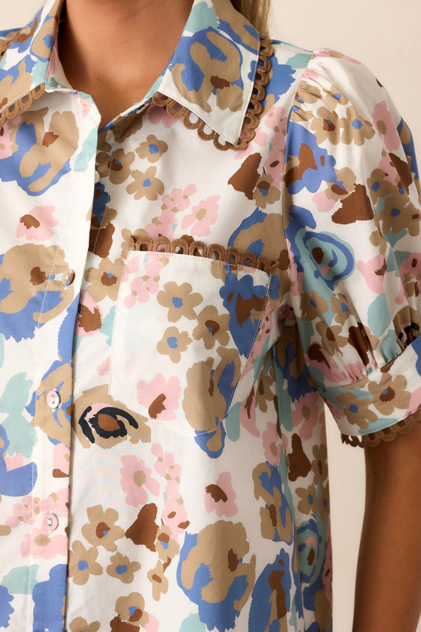 Close-up view of this ivory floral top that features a collar with brown detailing, puff sleeves, a front functional pocket and a functional button-front.