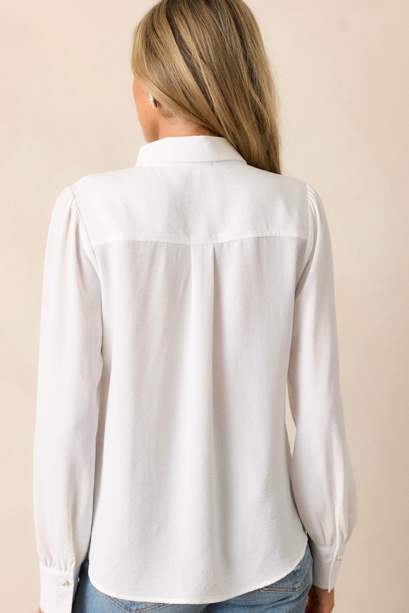 Back view of an ivory top that features a collared neckline, two faux pearls on the neckline, cuffed long balloon sleeves and a light breathable fabric.