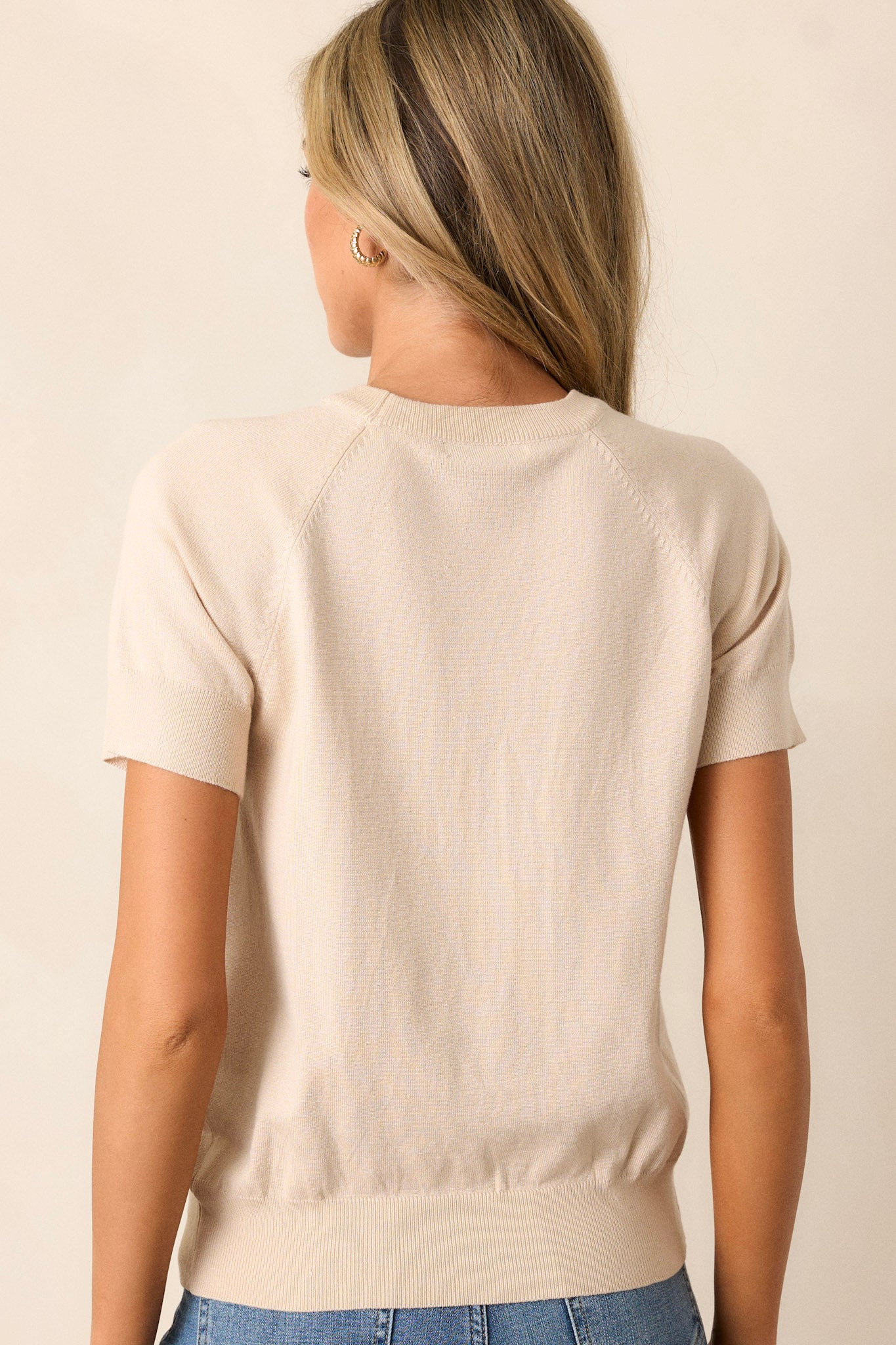 Back view of a beige sweater top highlighting the overall fit, soft material, and ribbed hemline