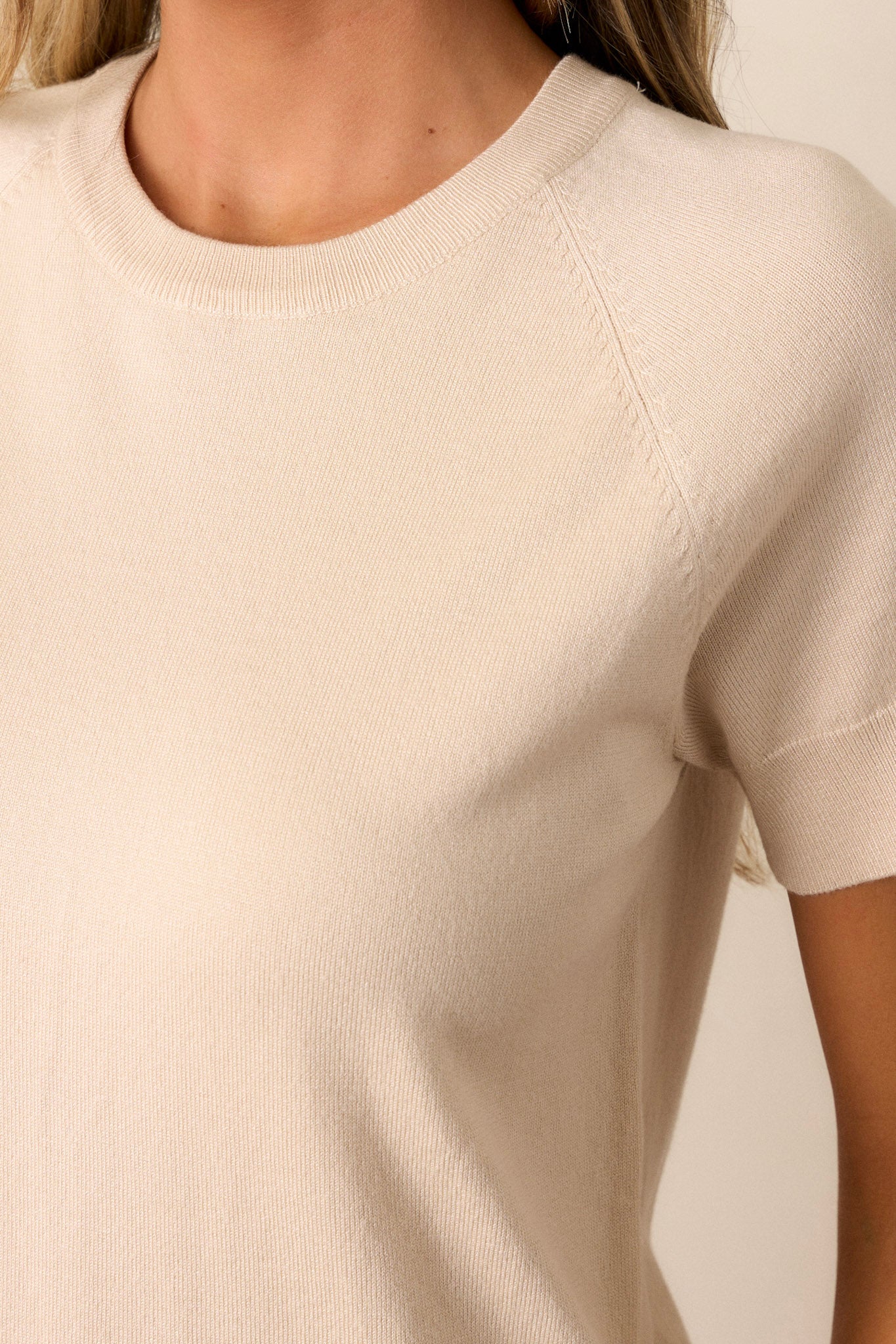 Close-up of the beige sweater top showing the ribbed crew neckline, seam detailing, and soft material.