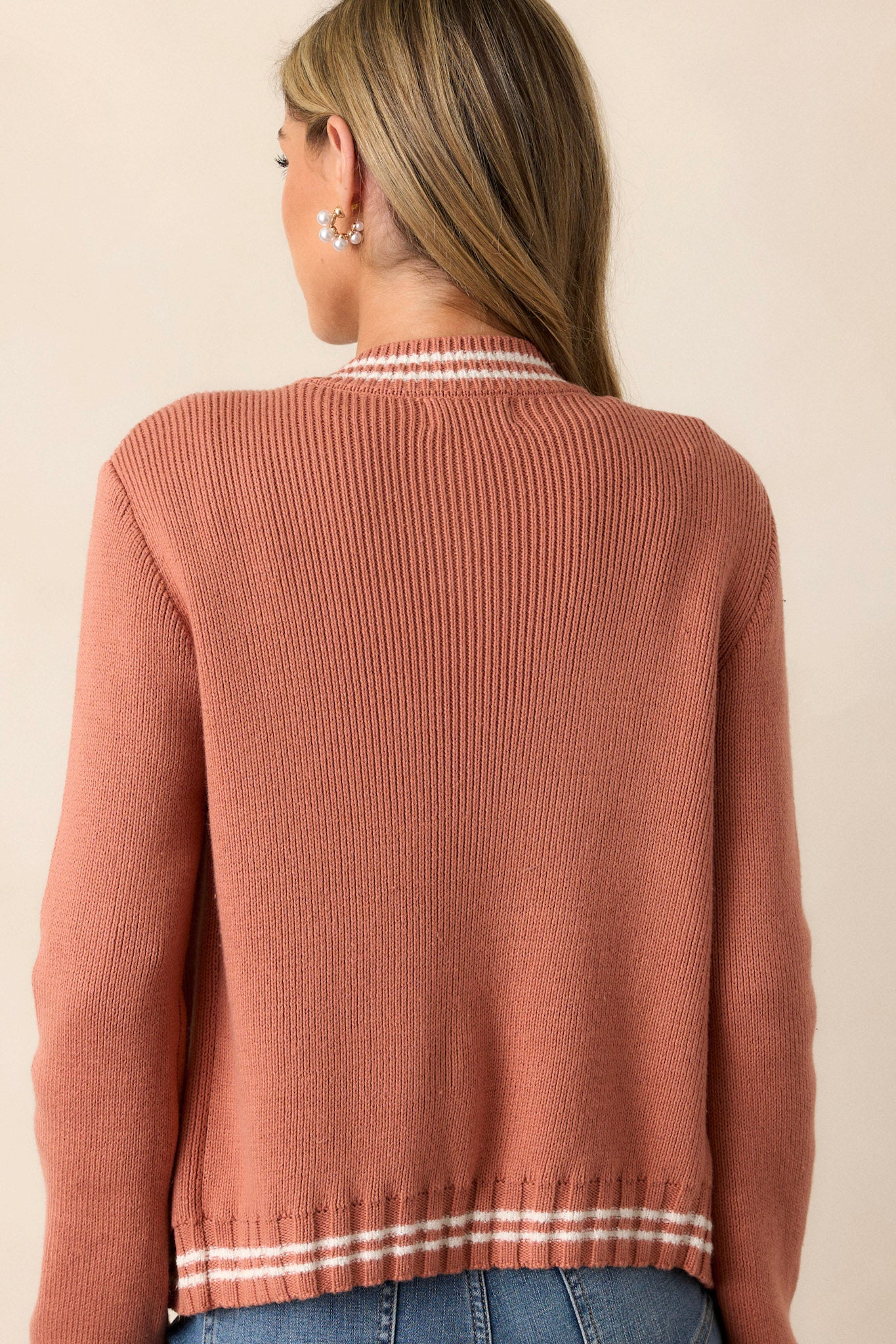 Back view of this terracotta knit cardigan that features a rounded neckline, a functional button front, a white stripe trim on the neckline, cuffs of the sleeves & the hemline, a soft knit texture and long sleeves.