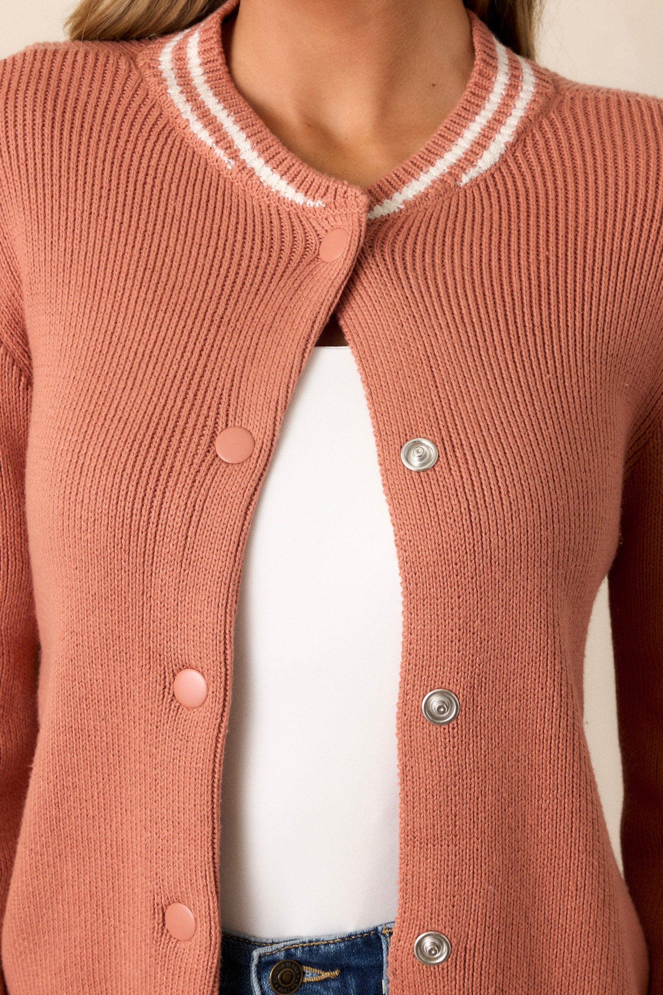 Close-up of this terracotta knit cardigan that features a rounded neckline, a functional button front, a white stripe trim on the neckline, cuffs of the sleeves & the hemline, a soft knit texture and long sleeves.