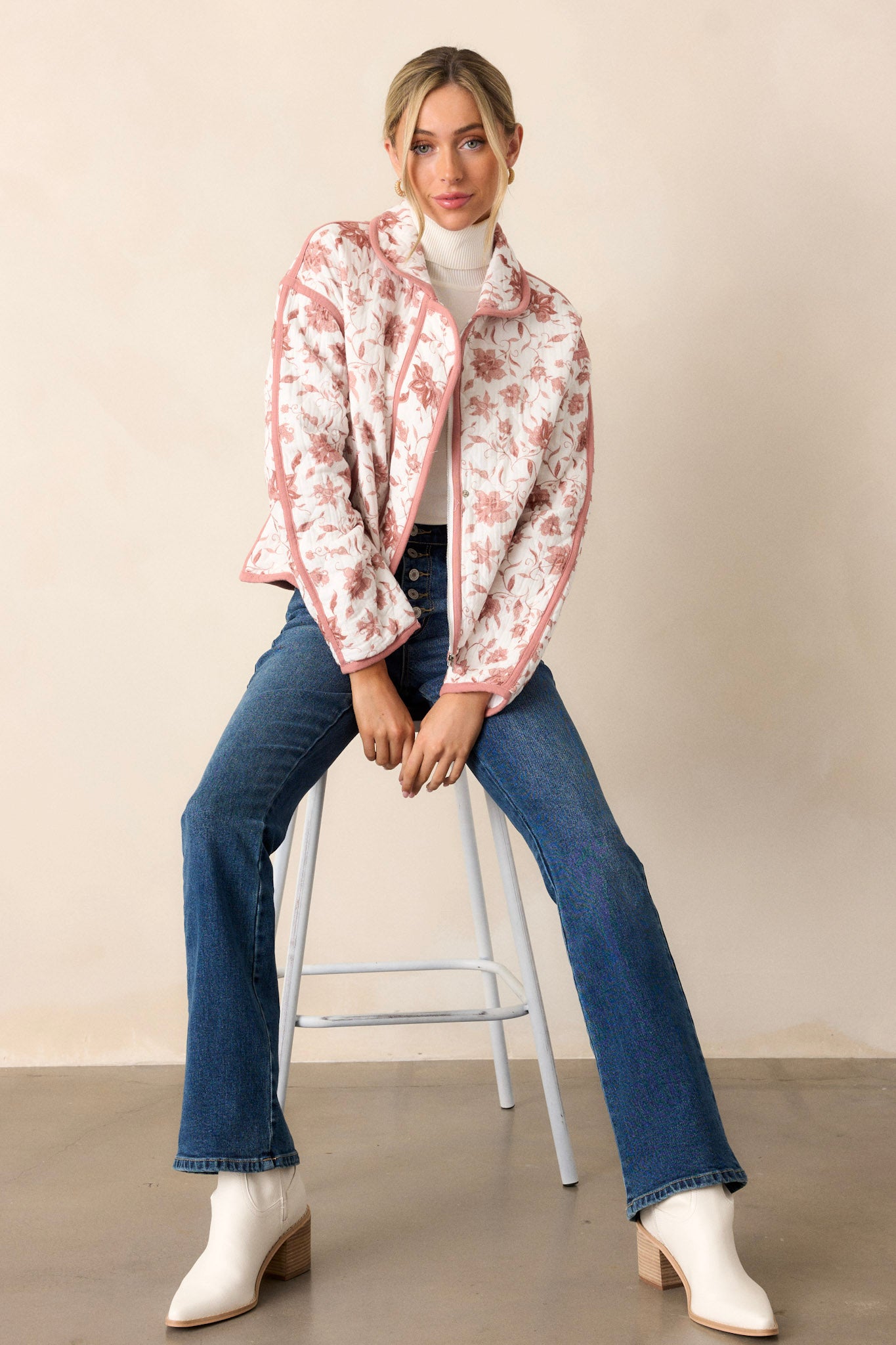 Seated view of this dusty pink jacket that features a collared neckline, a full zip front, a solid dusty pink trim, an ivory floral print, a soft quilted material and snap buttons for extra support.