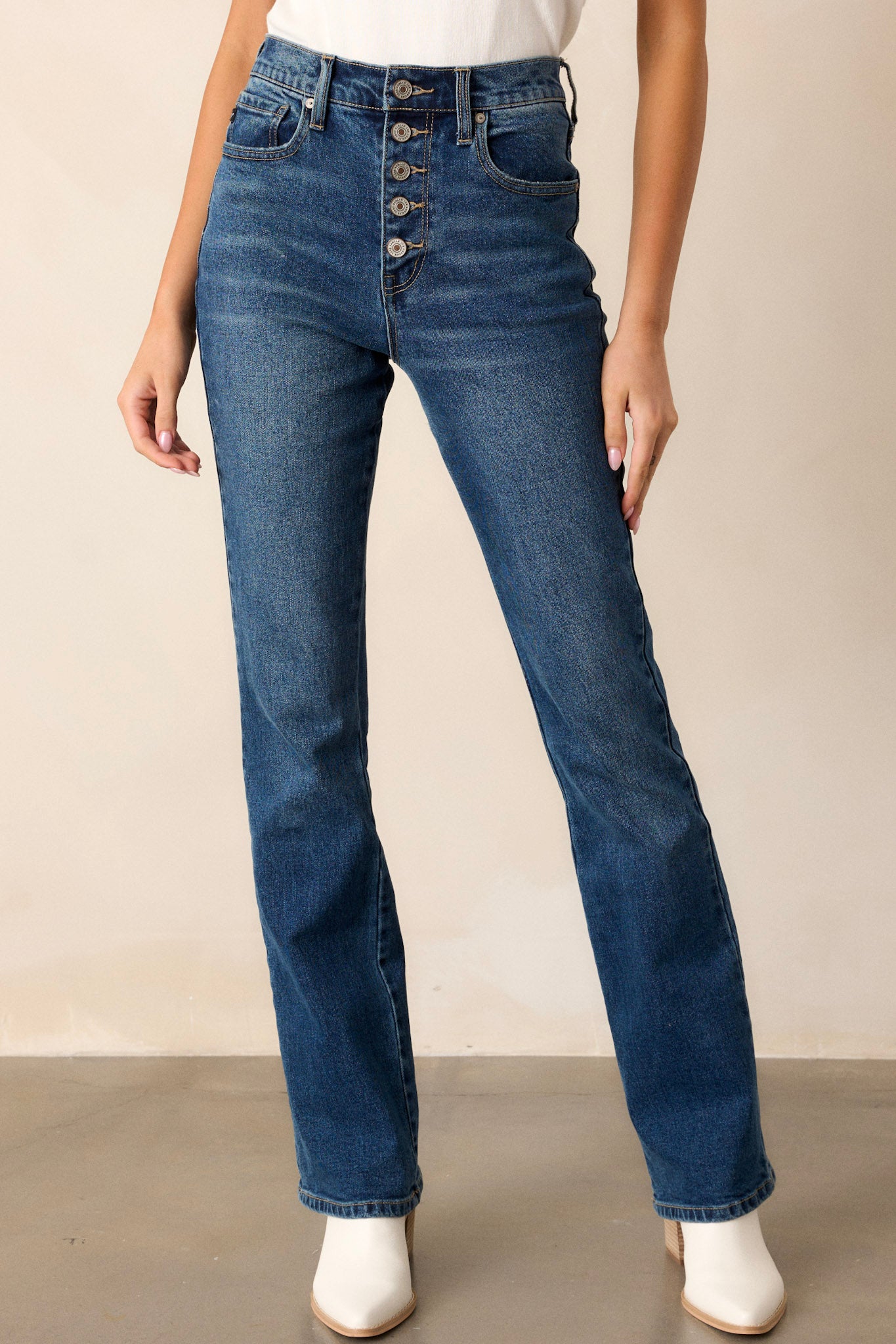 Front view of these dark wash jeans featuring a high waist with a butterfly button detail, functional belt loops and pockets, and a straight leg style.