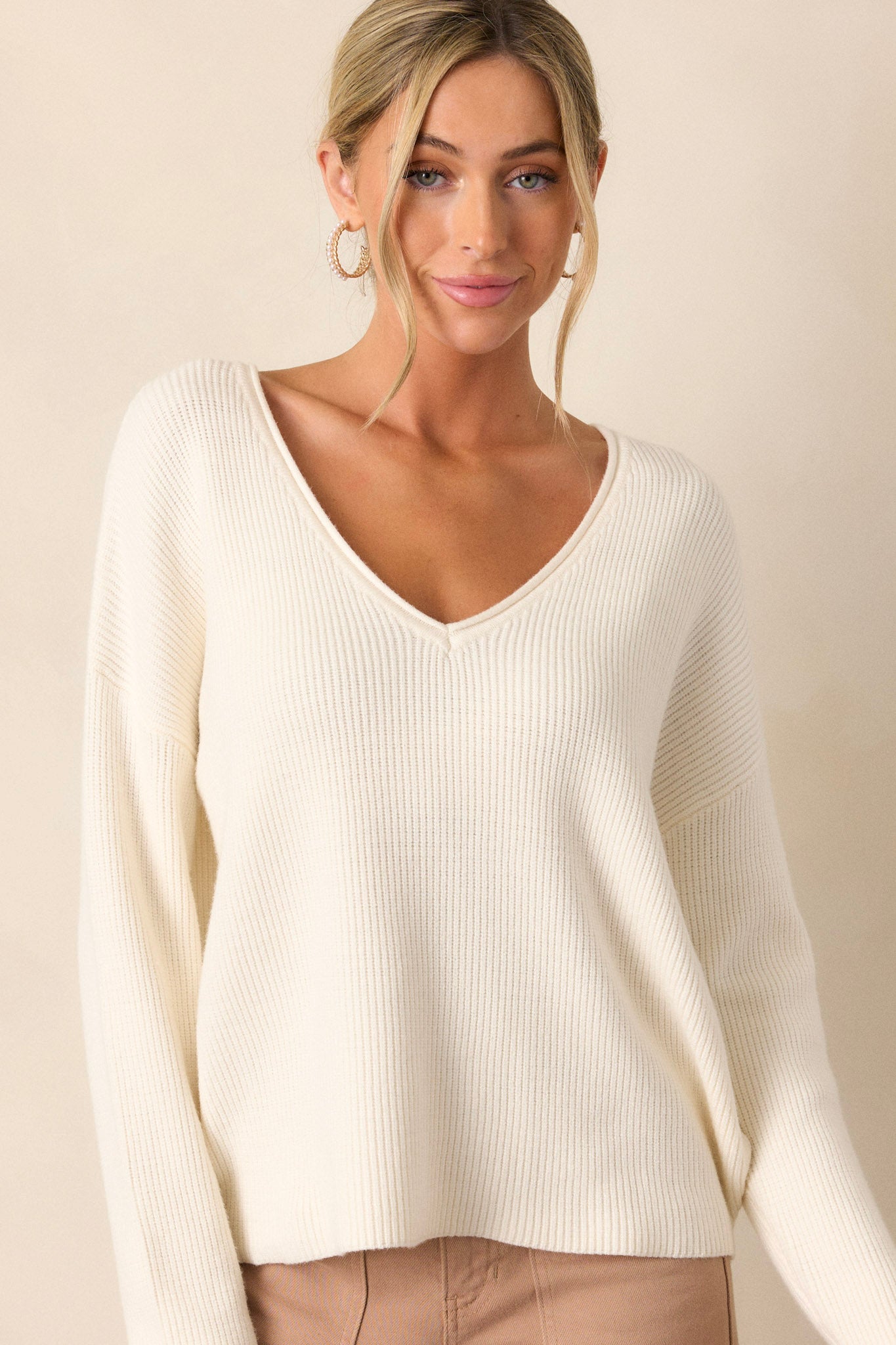 Untucked front view of an ivory sweater featuring a ribbed design, a v-neck and comfortable fabric.