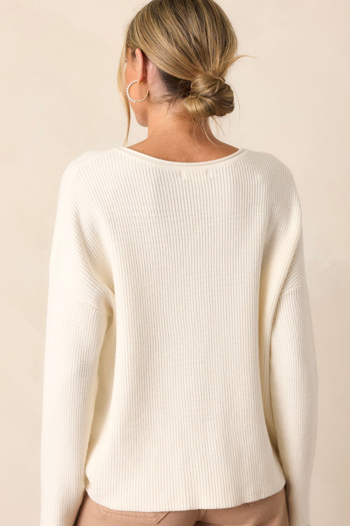 Back view of an ivory sweater featuring a ribbed design, a v-neck and comfortable fabric.