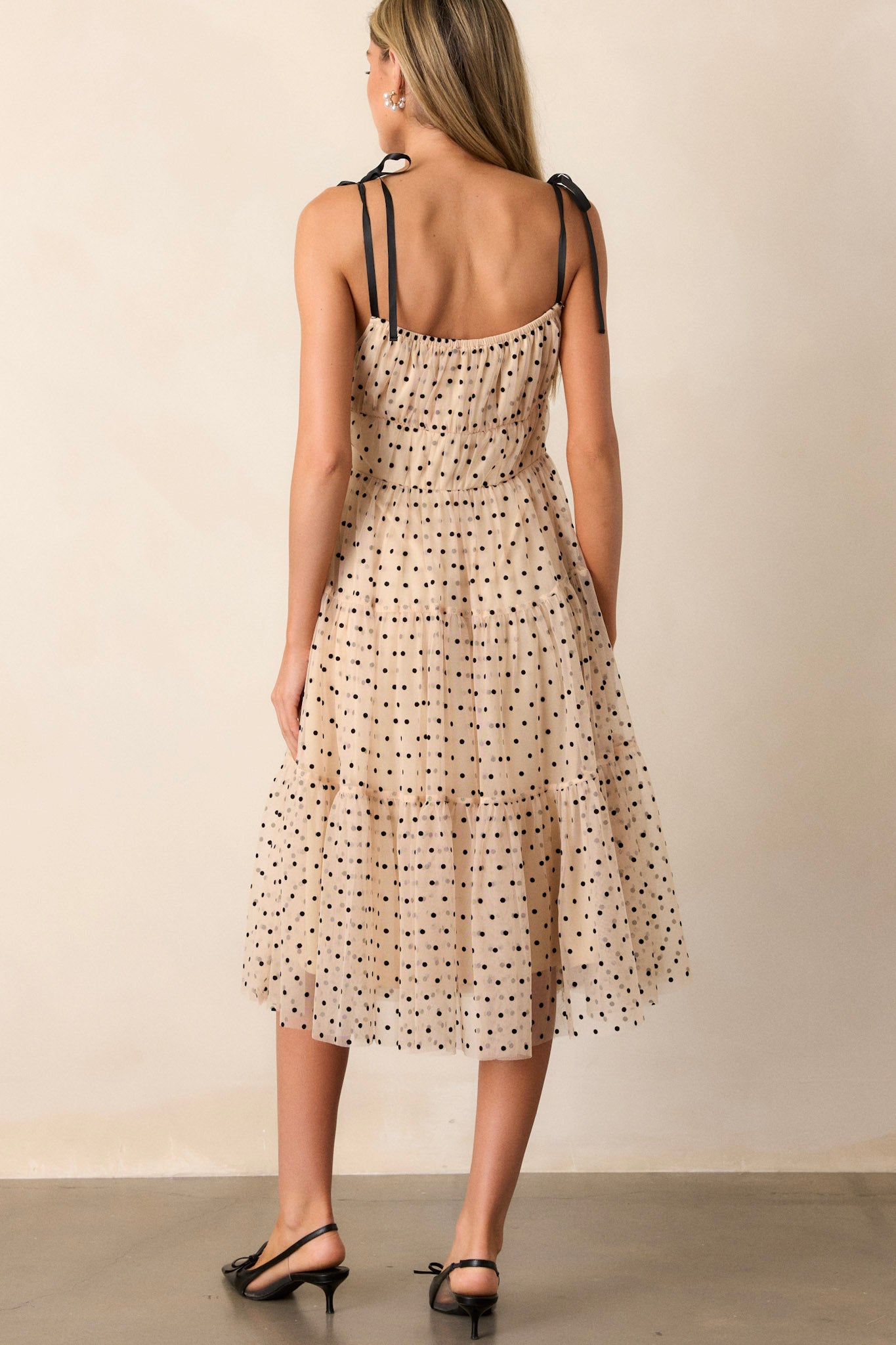 Back view of a beige midi dress highlighting the thin self-tie straps, tiers, black polka dots, and tulle.