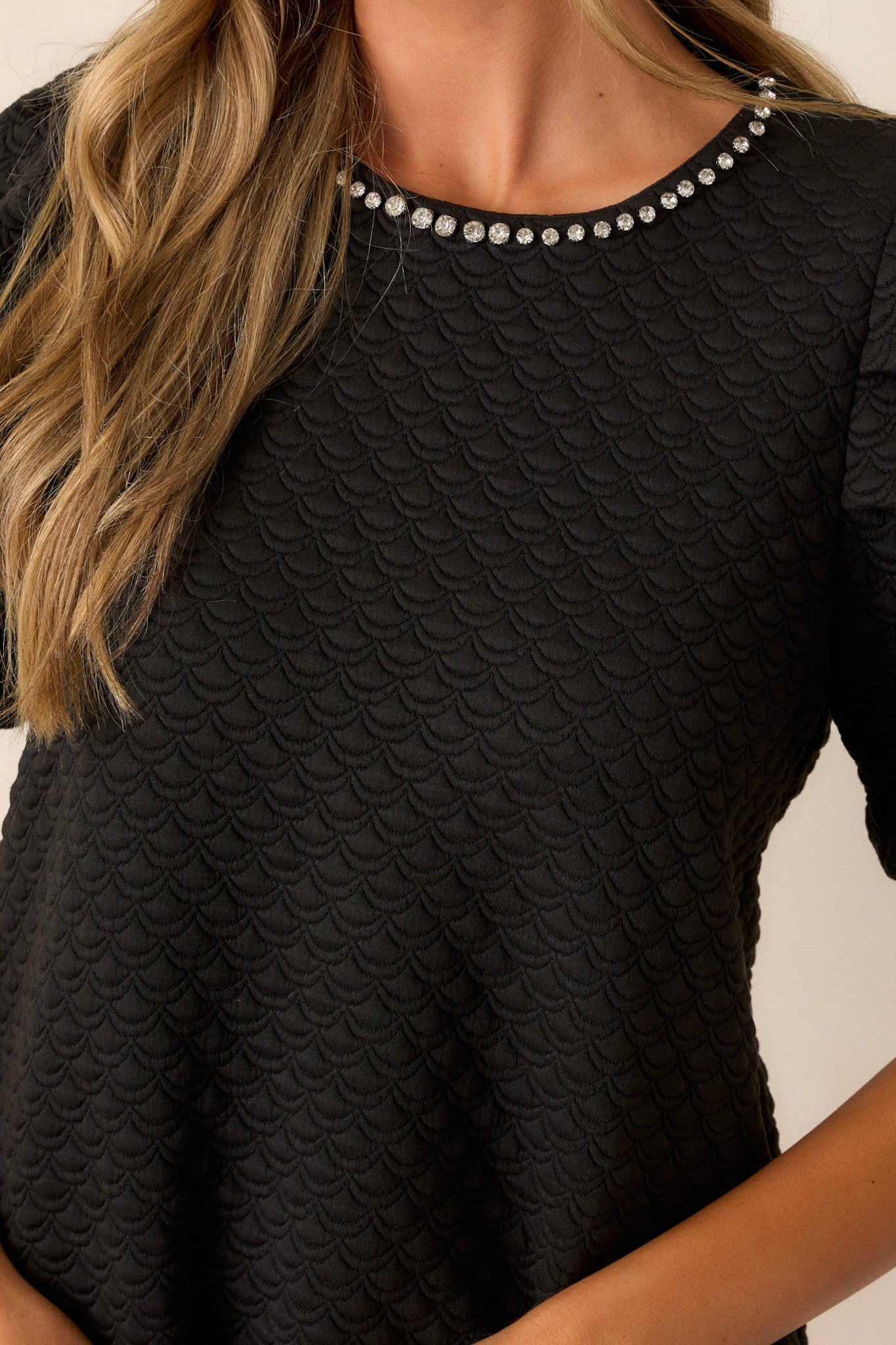 Close up view of the quilted scallop fabric and rhinestone collar detailing on this black mini dress.