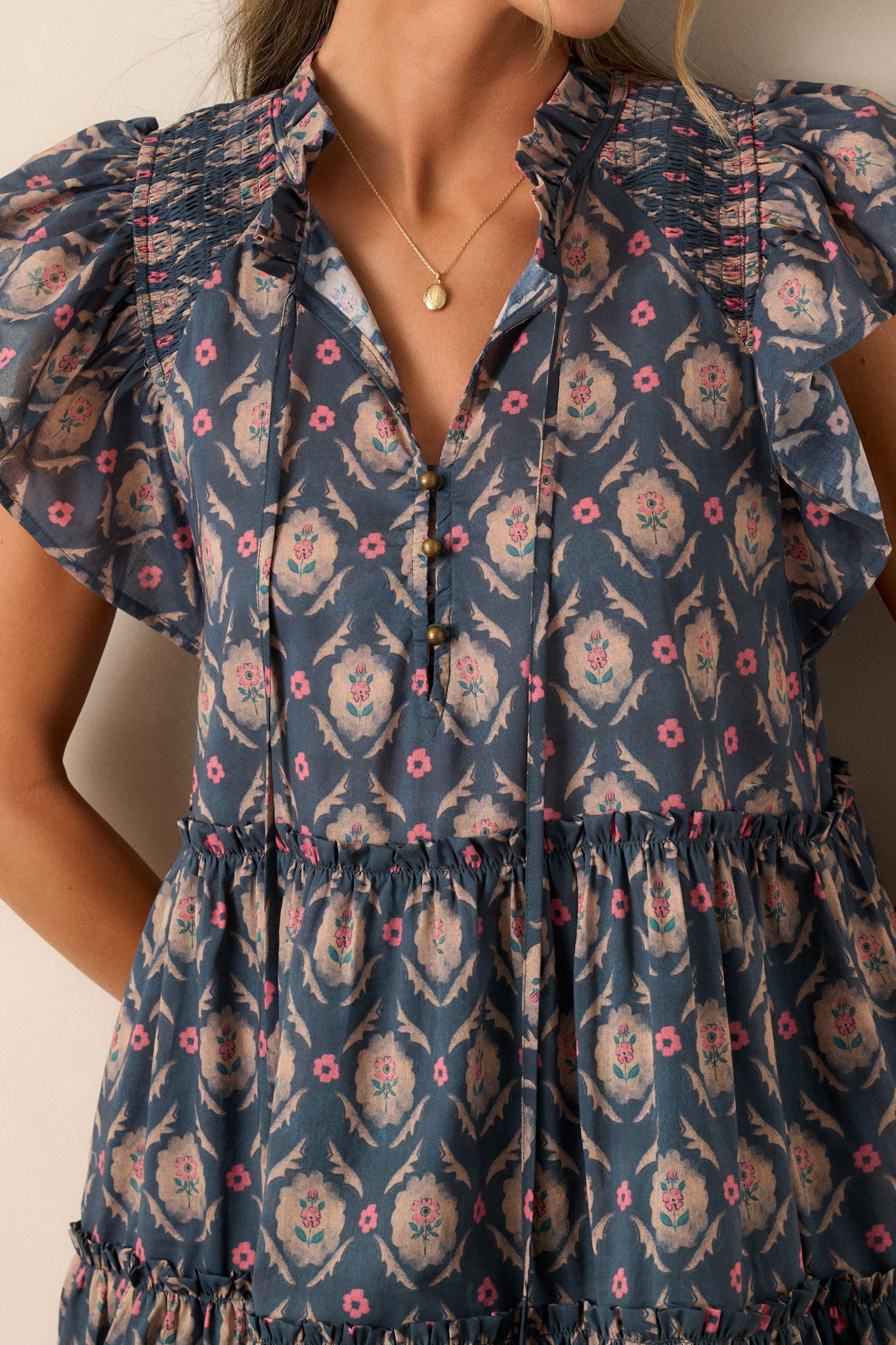 Close-up of this dark teal dress that features a ruffled split neckline, a tiered design, flutter sleeves, functional pockets and a floral print.