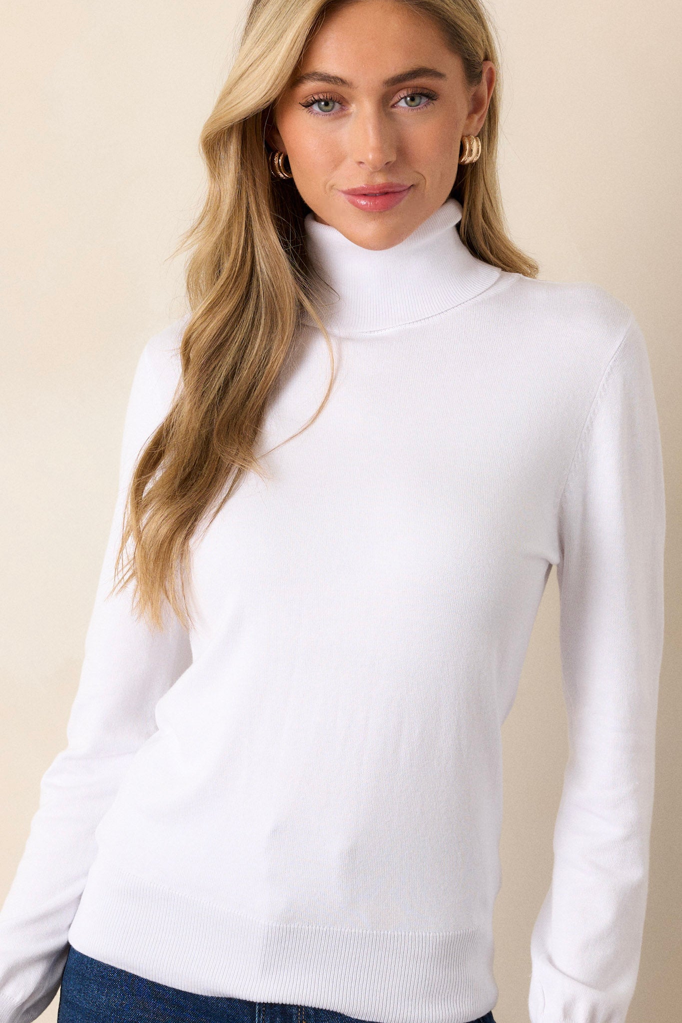 A white sweater featuring a turtle neckline, long sleeves with ribbed cuffs, and a ribbed bottom hem that tapers in.