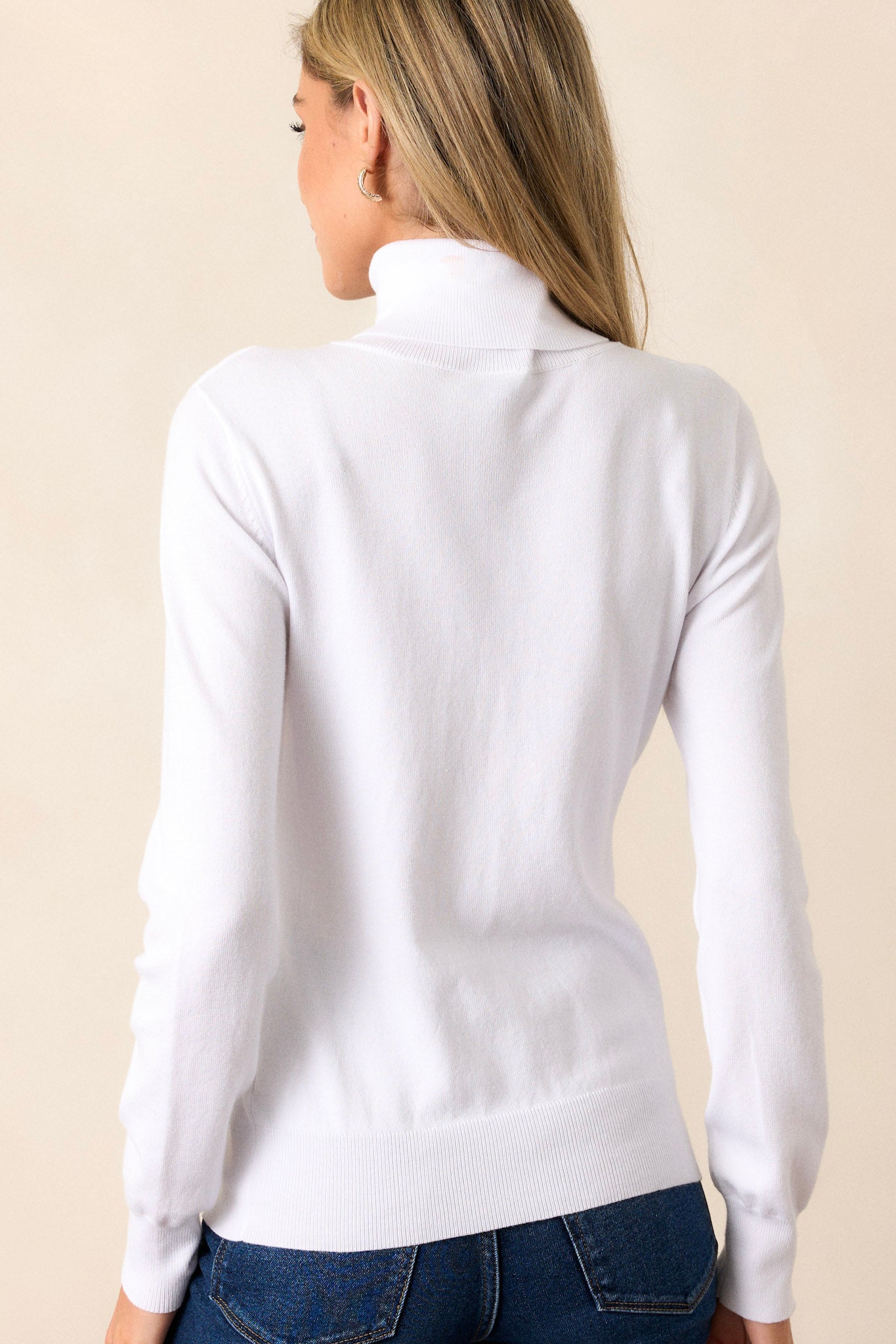 Back view of the white sweater featuring long sleeves with ribbed cuffs and a ribbed bottom hem that tapers in.