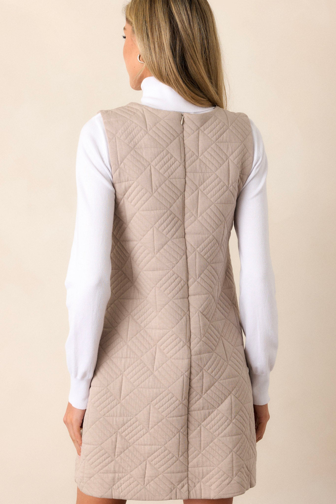 Back view of a taupe mini dress highlighting the overall fit, quilted fabric, and sleeveless design.