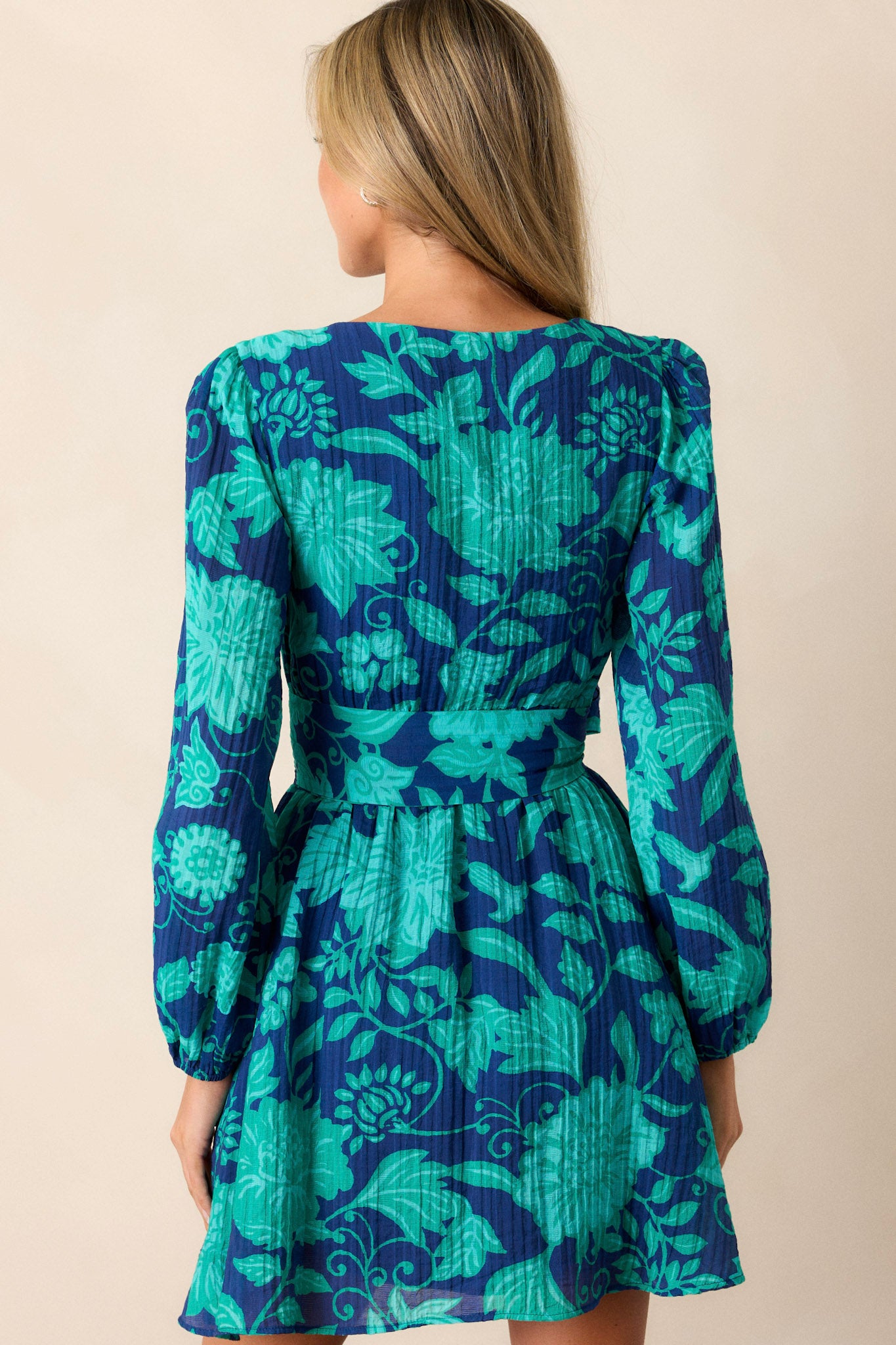 A view of the back of the dress, highlighting the long sleeves with elastic cuffs and how the floral pattern and waist belt wrap around the back, with the fabric flowing toward the skirt.