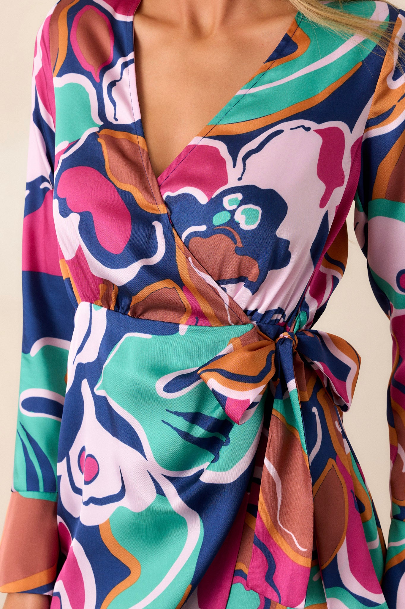 Close-up of this floral dress that features a v-neckline, long sleeves, a self-tie belt, and a fun floral print.