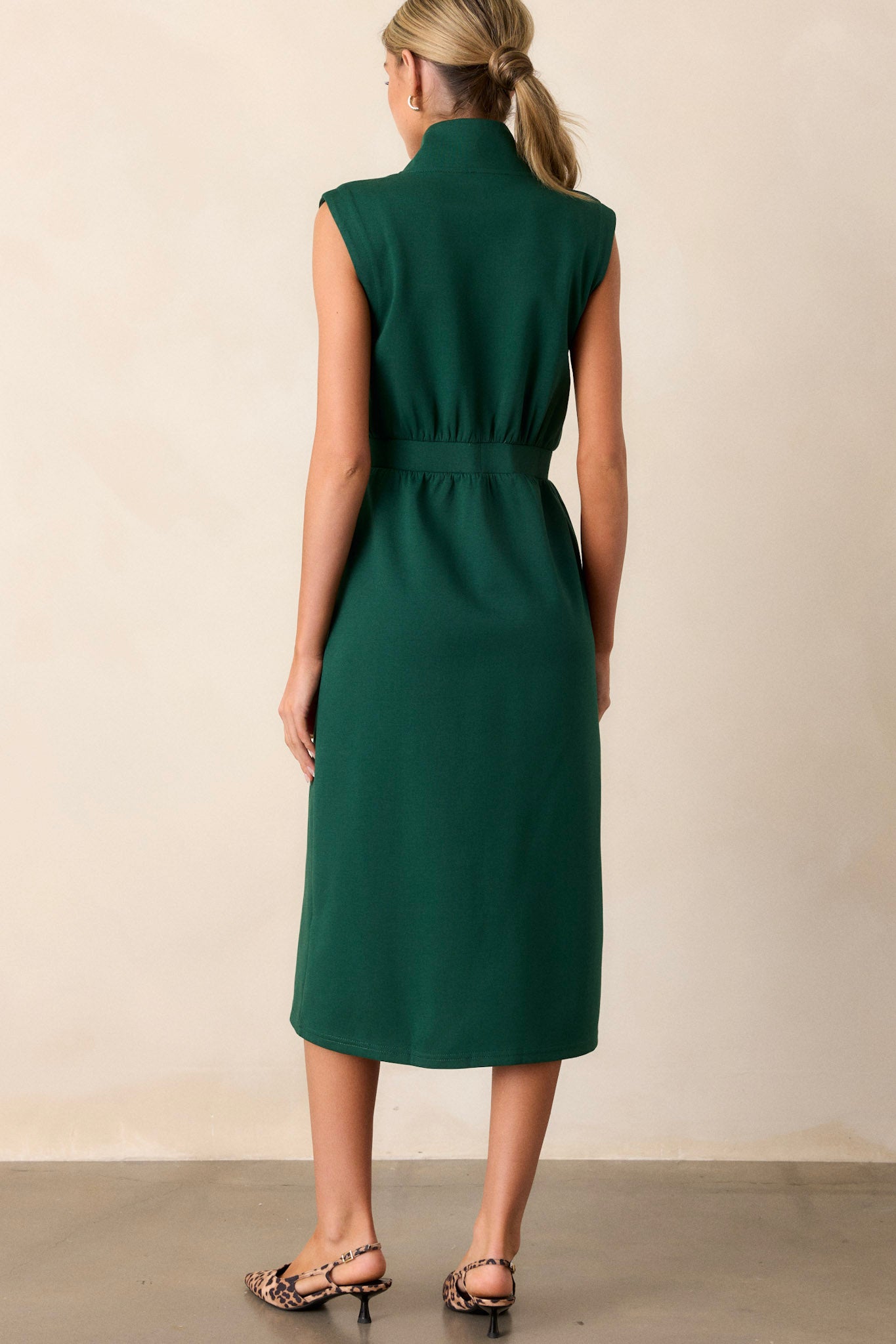 Back view of this hunter green dress that features a v-neckline, a slight collar, a zipper front, functional hip pockets, a middle split in the hem and a sleeveless design.