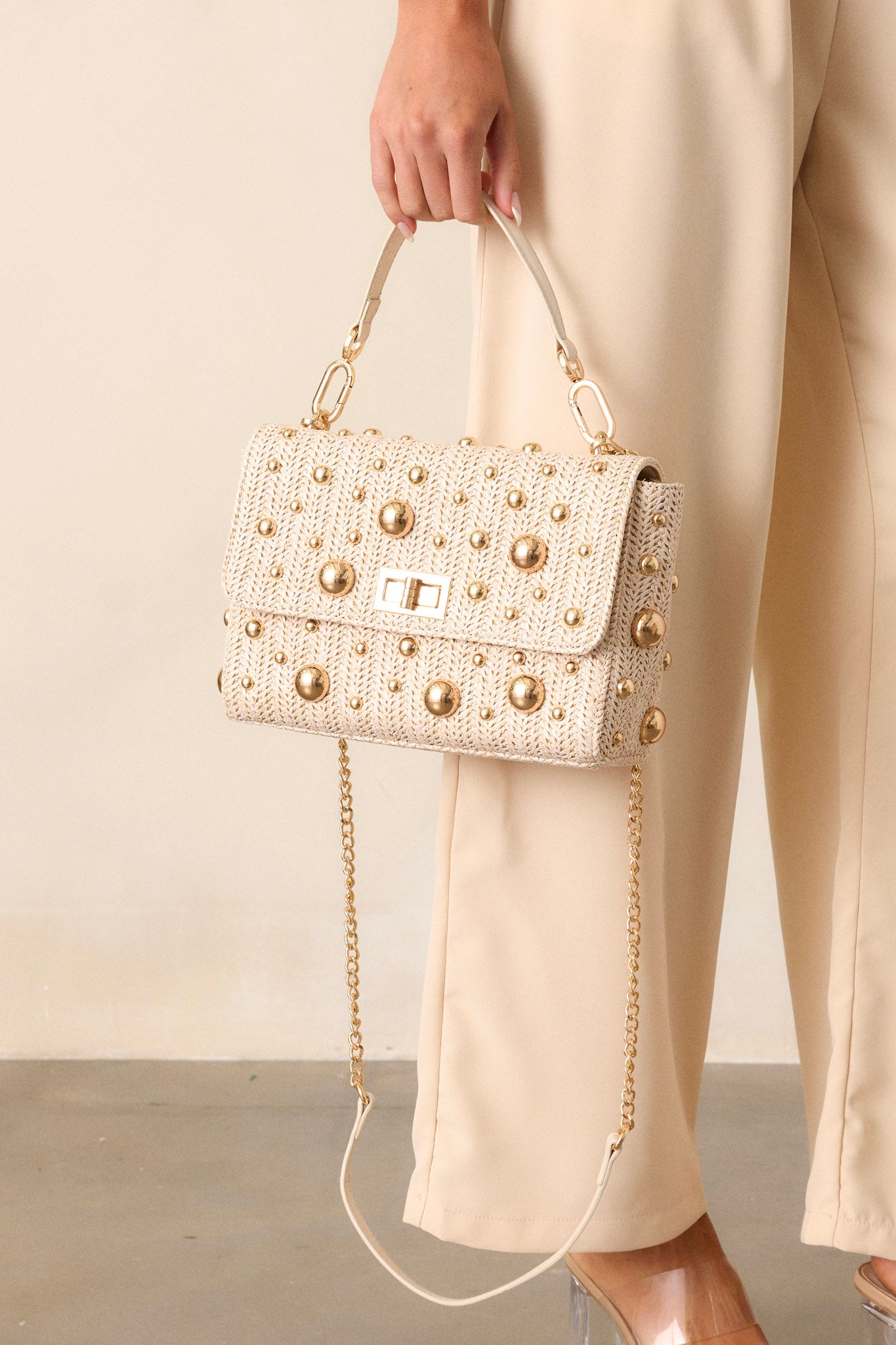 Full view of this rattan handbag that features a square shape, gold reflective polka dots, a gold turn closure, gold hooks for optional strap and a zippered pouch inside.