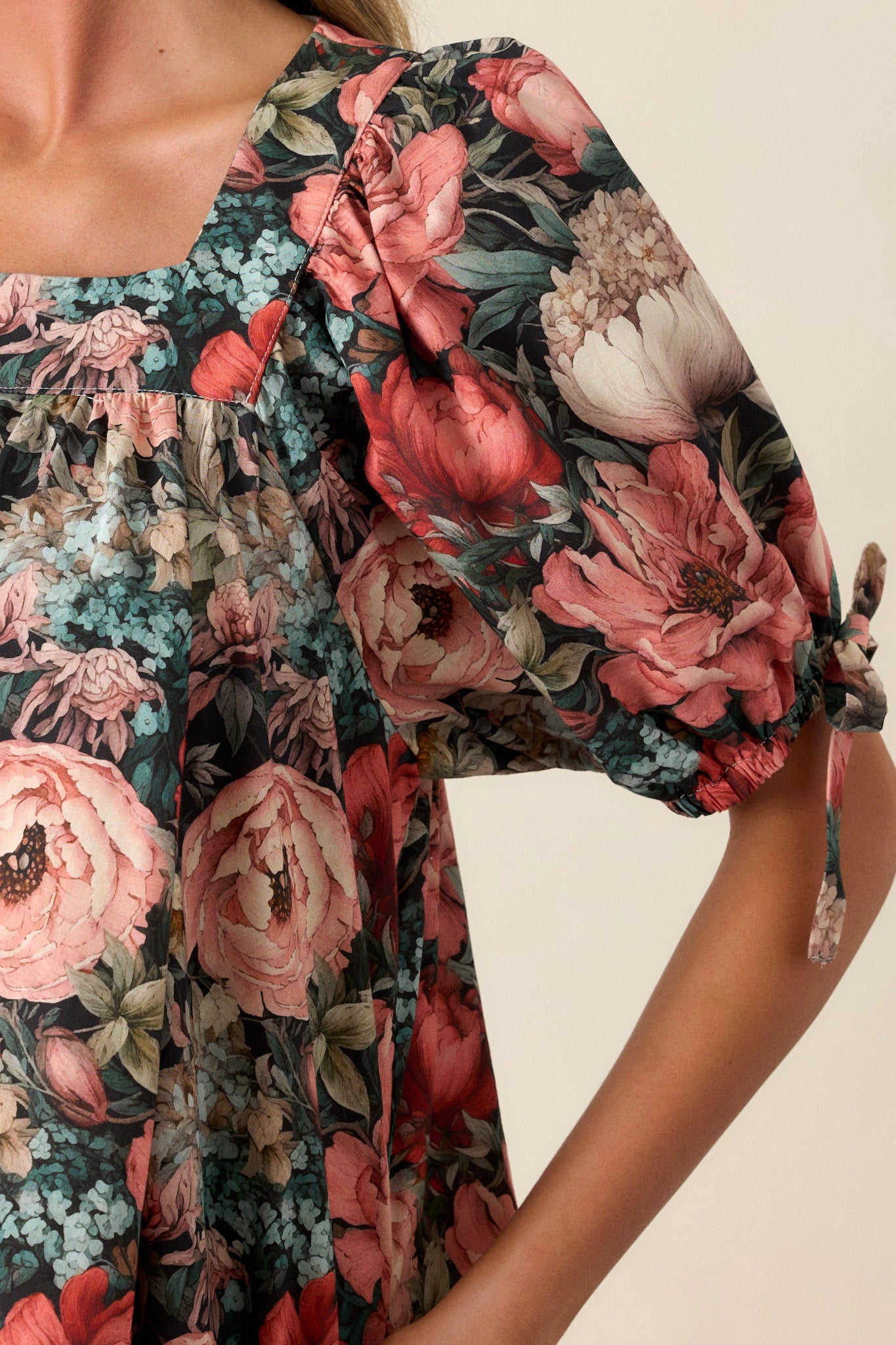 Close-up of the black floral dress focusing on the square neckline, puff sleeves, and the fabric pattern near the two functional side pockets.