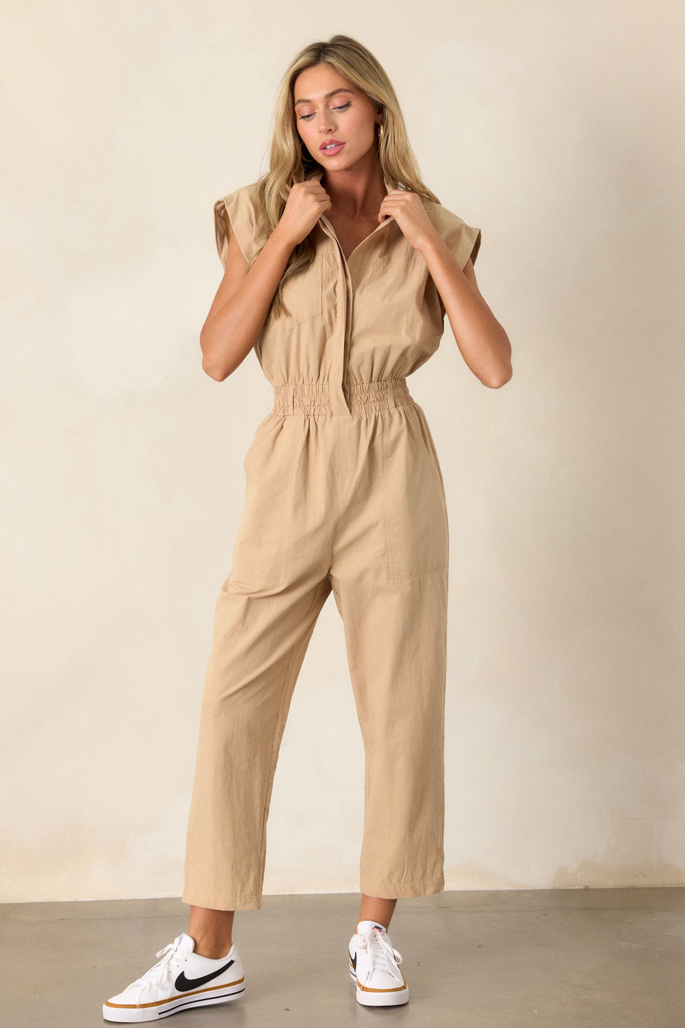 Front angled view of a jumpsuit featuring two side pockets, a stretchy soft waistband, and a popped collar