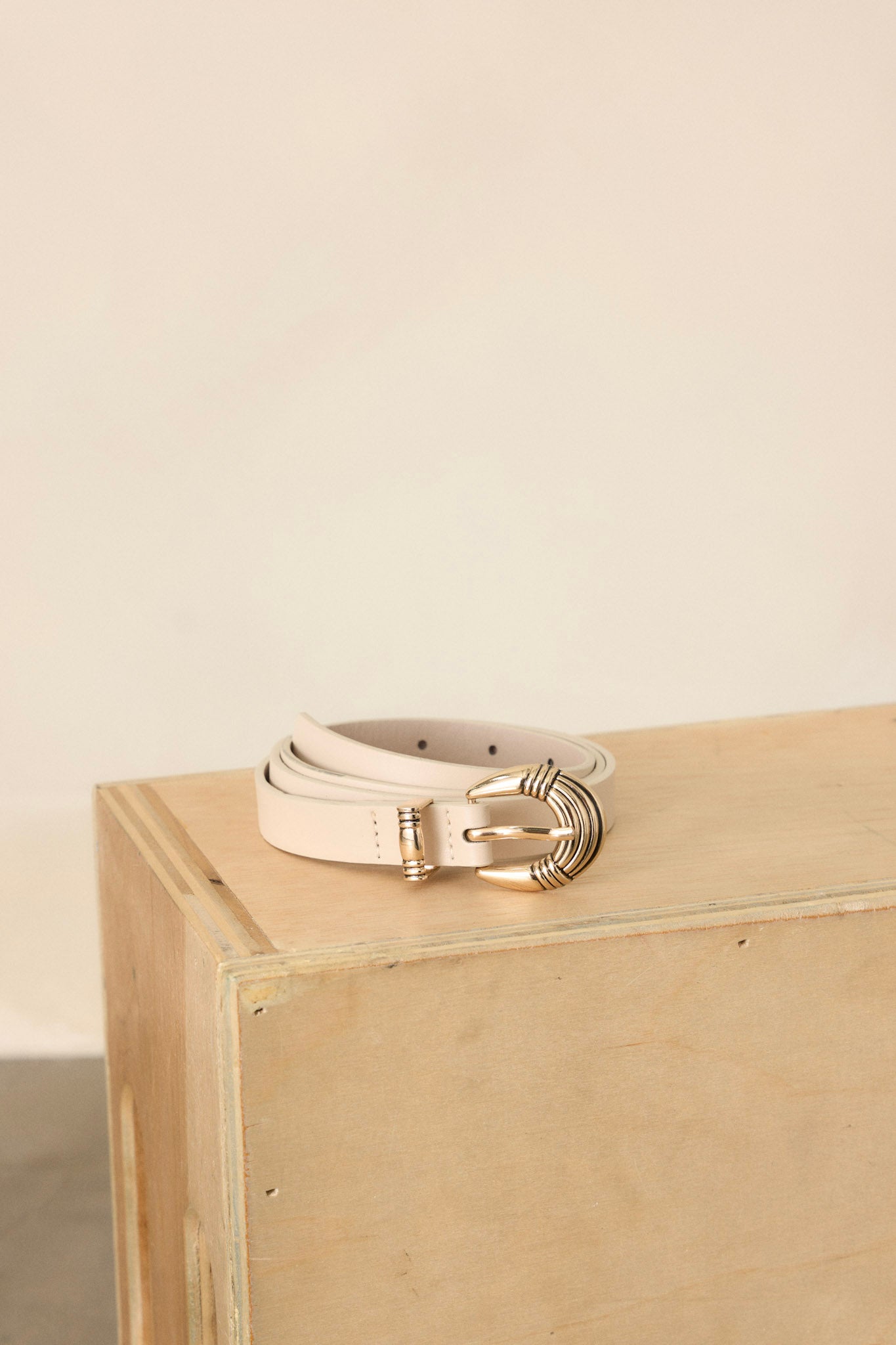 An ivory faux leather belt neatly coiled, displayed on a wooden surface. 