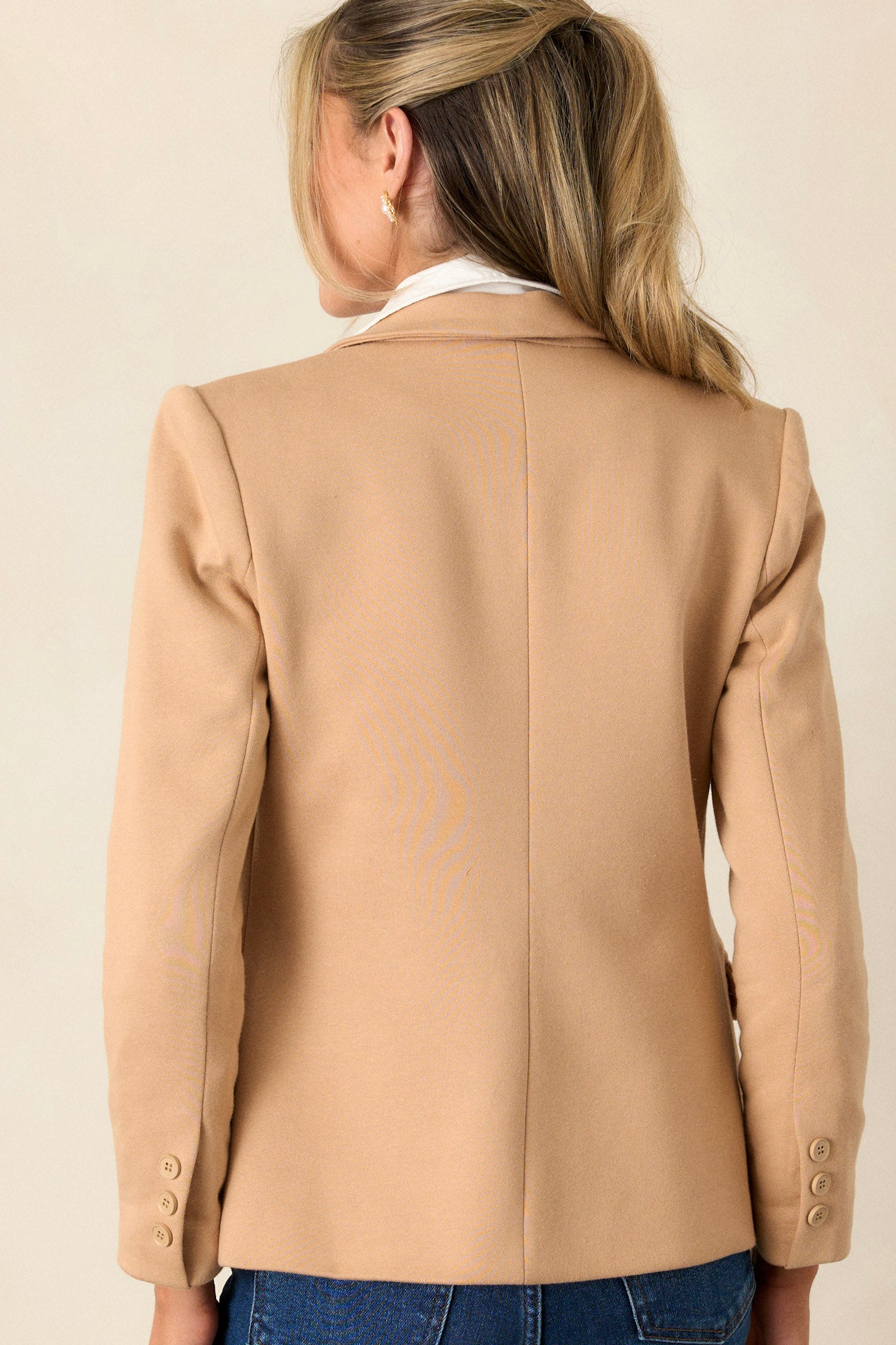 Back view of this blazer that features a notch lapel collar, shoulder pads, a functional button, faux pockets, and faux buttons on the sleeves.